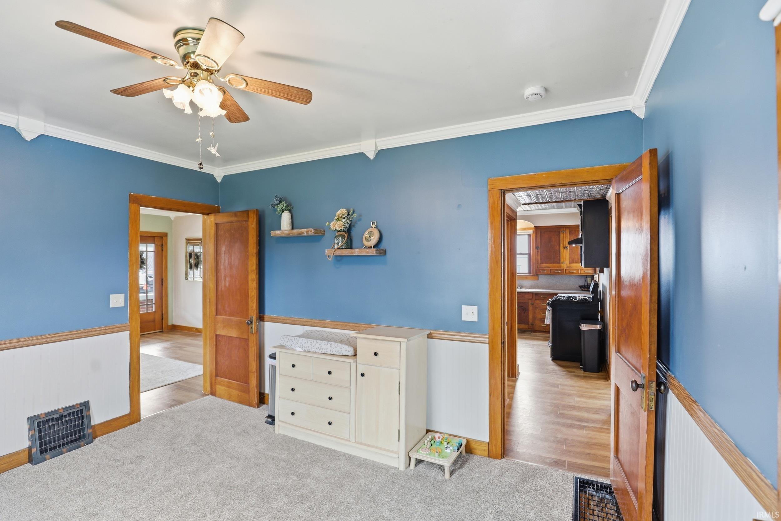 Bedroom with a wainscoted wall, crown molding, light colored carpet, and ceiling fan