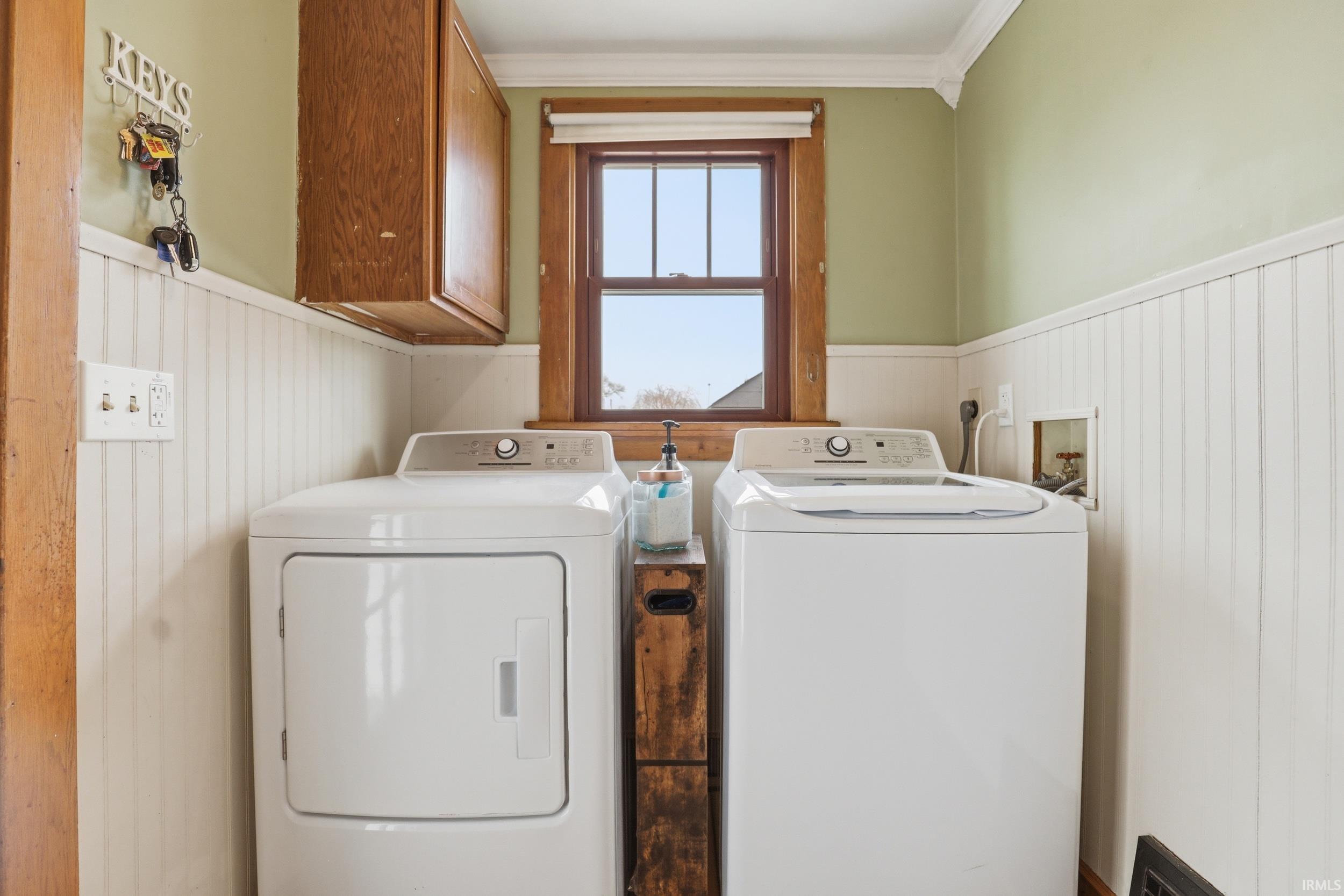 Laundry area with a wainscoted wall, cabinet space, washing machine and dryer, and ornamental molding