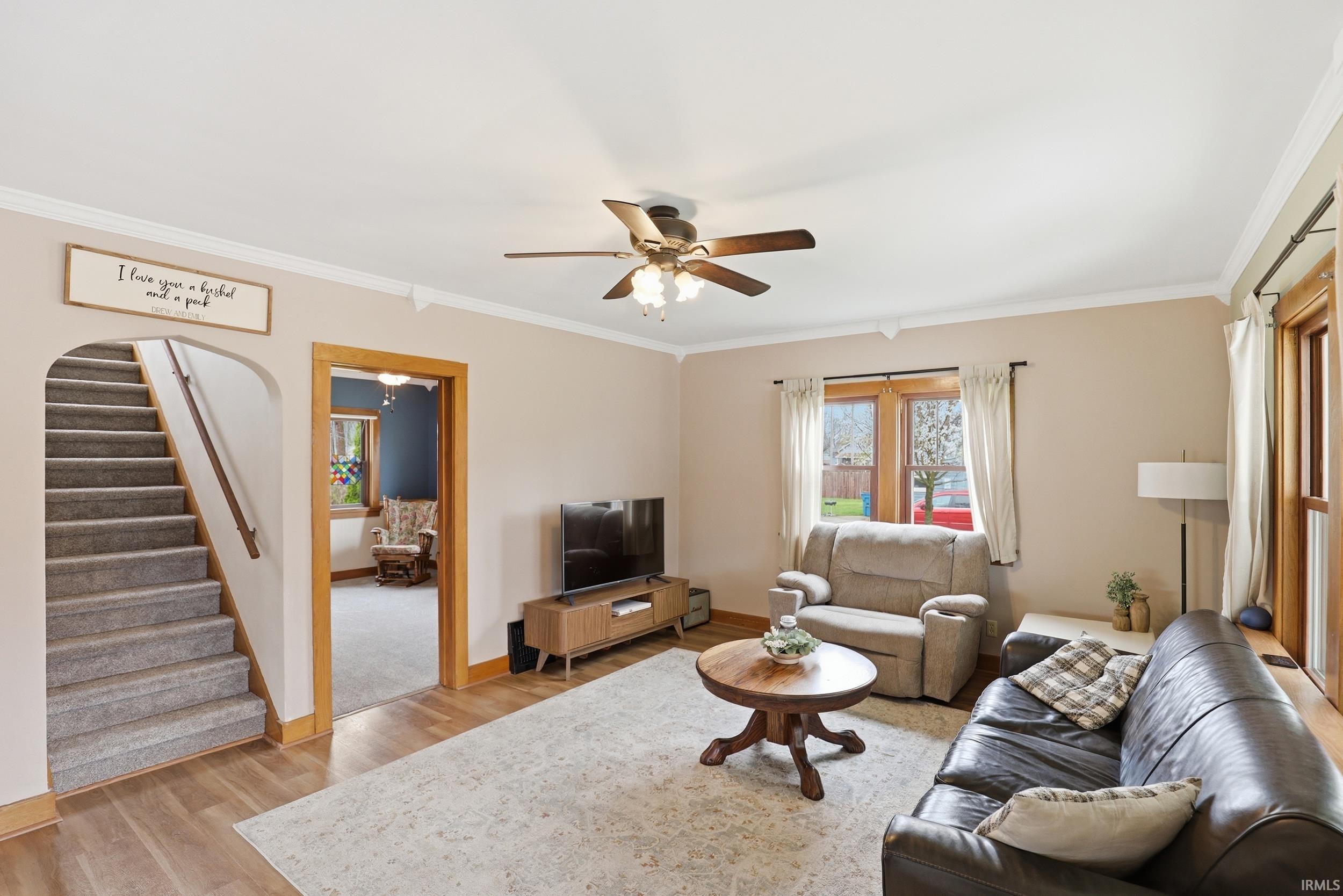 Living area with ornamental molding, ceiling fan, and light wood-style flooring