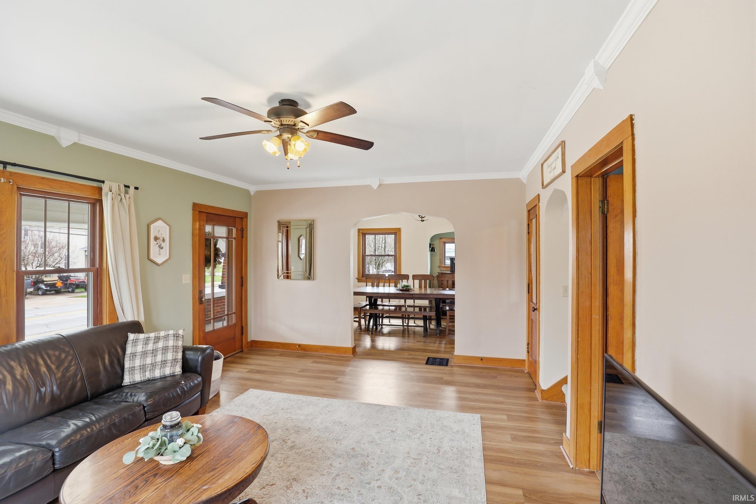 Living area with a ceiling fan, light wood-type flooring, arched walkways, and ornamental molding
