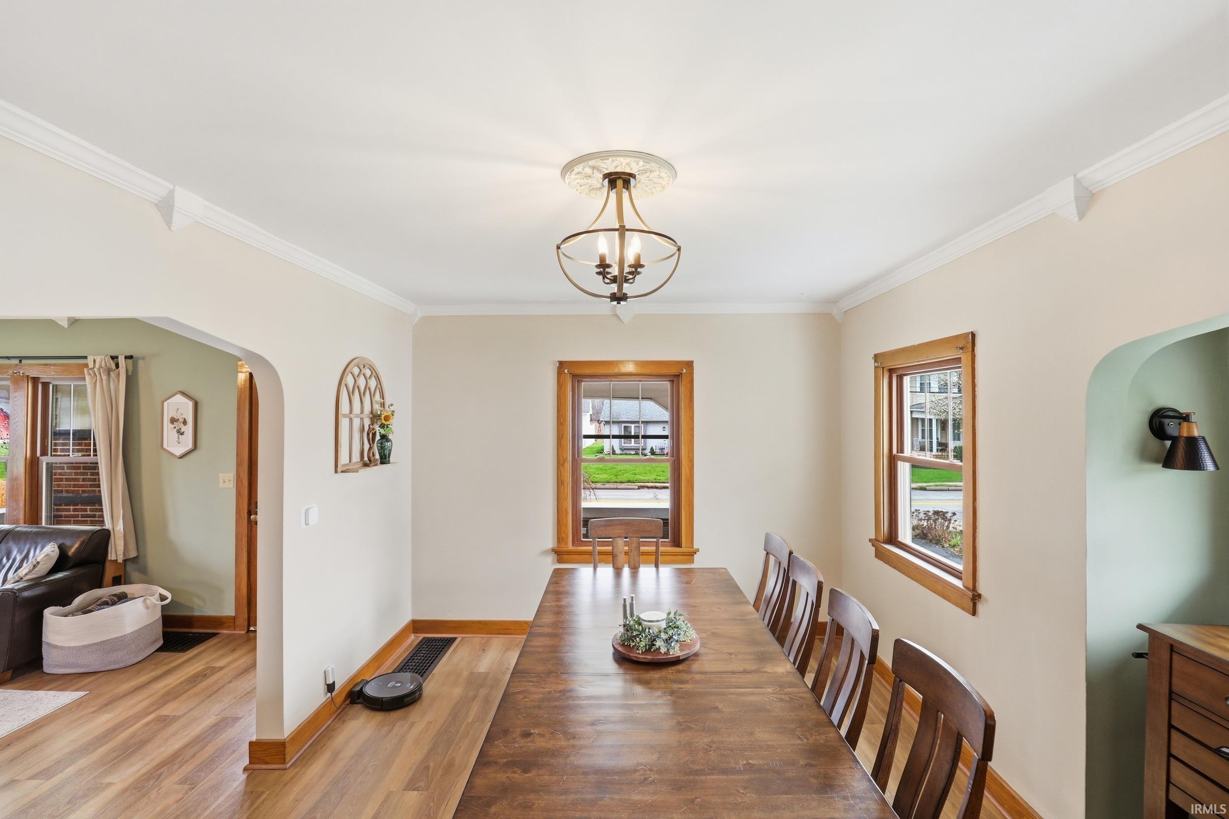 Dining space featuring arched walkways, light wood-style flooring, a chandelier, and ornamental molding