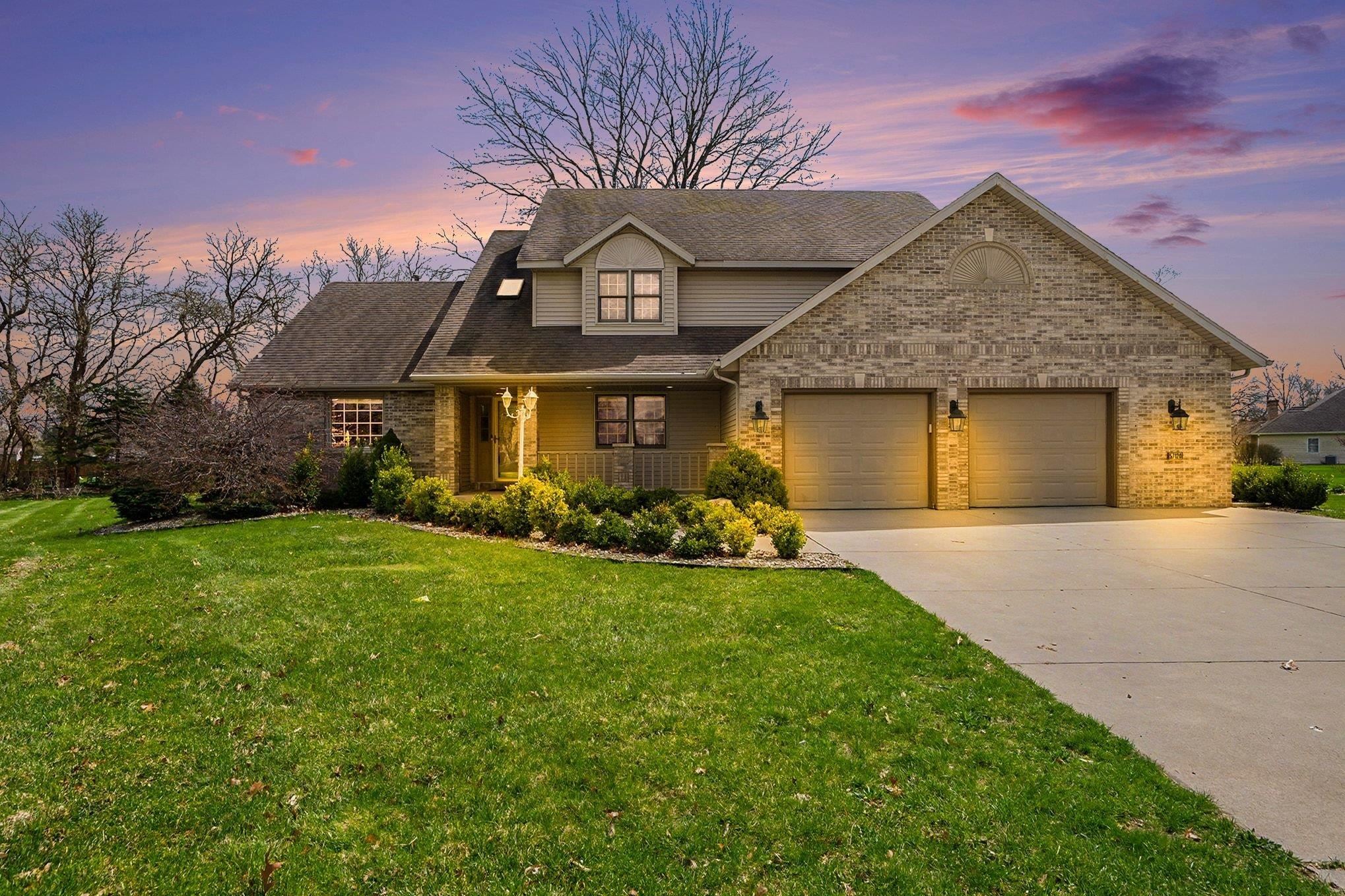 View of front of property with brick siding, a porch, concrete driveway, a lawn, and a garage