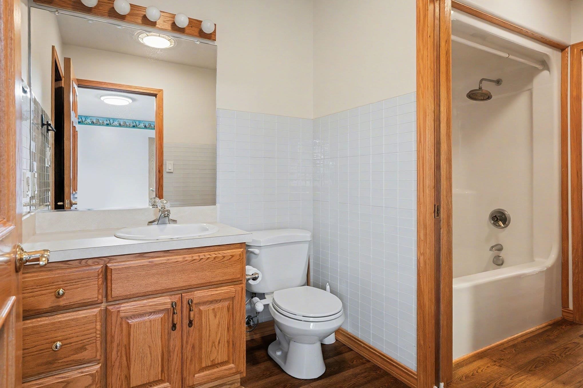 Bathroom featuring vanity, dark wood-style flooring, washtub / shower combination, and tile walls