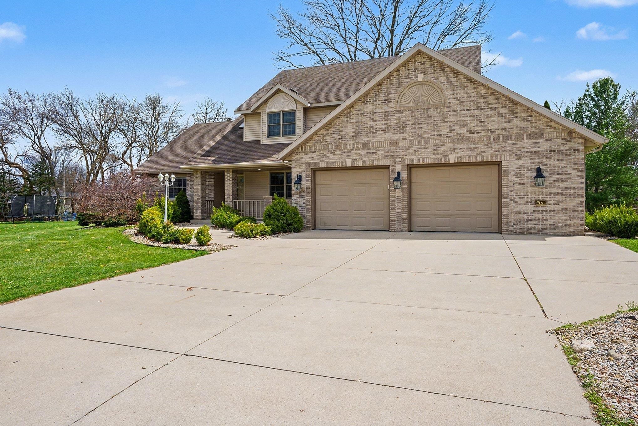 View of front of home featuring a front yard, concrete driveway, a porch, a shingled roof, and brick siding