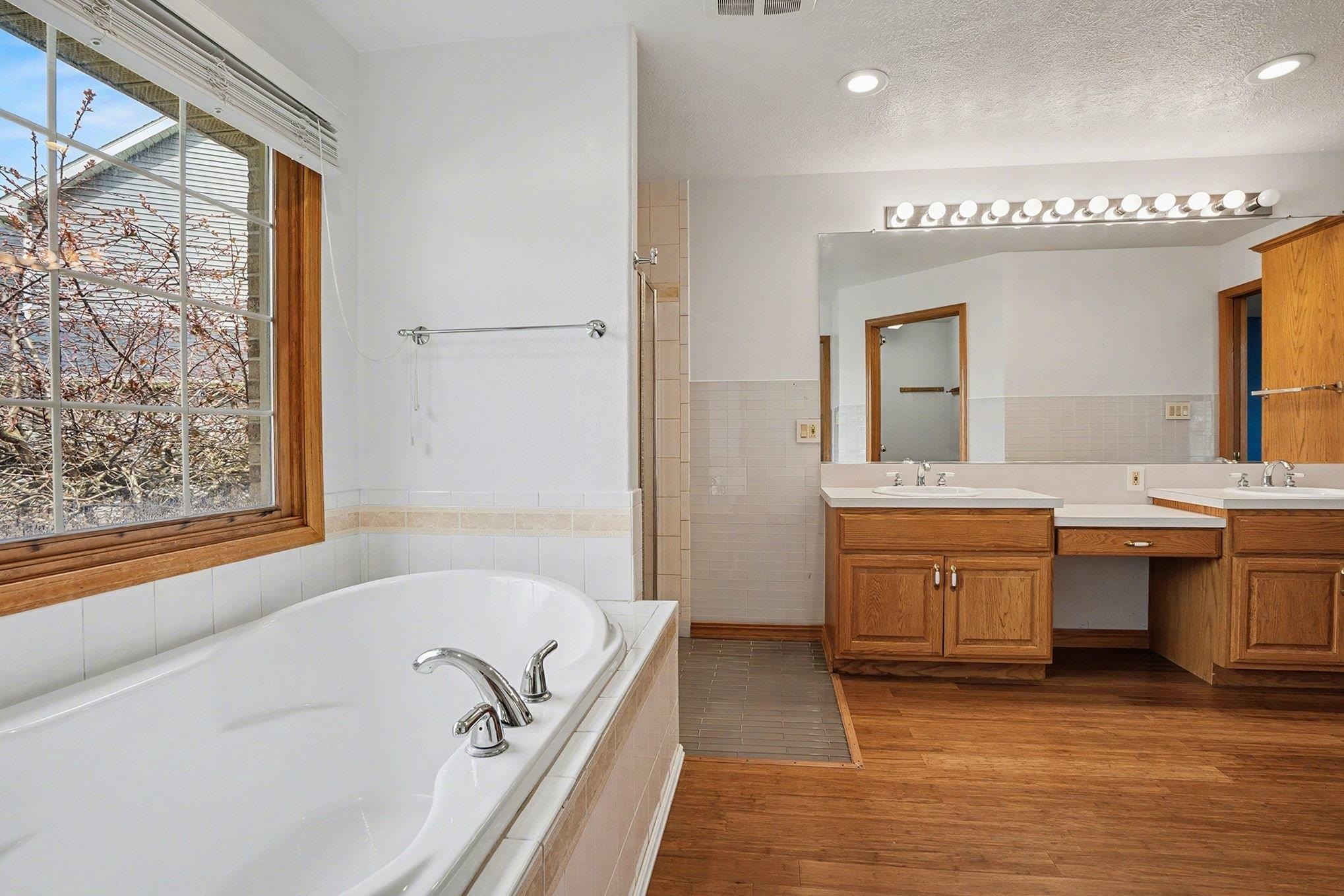 Full bathroom with double vanity, a garden tub, dark wood-style floors, tile walls, and a textured ceiling