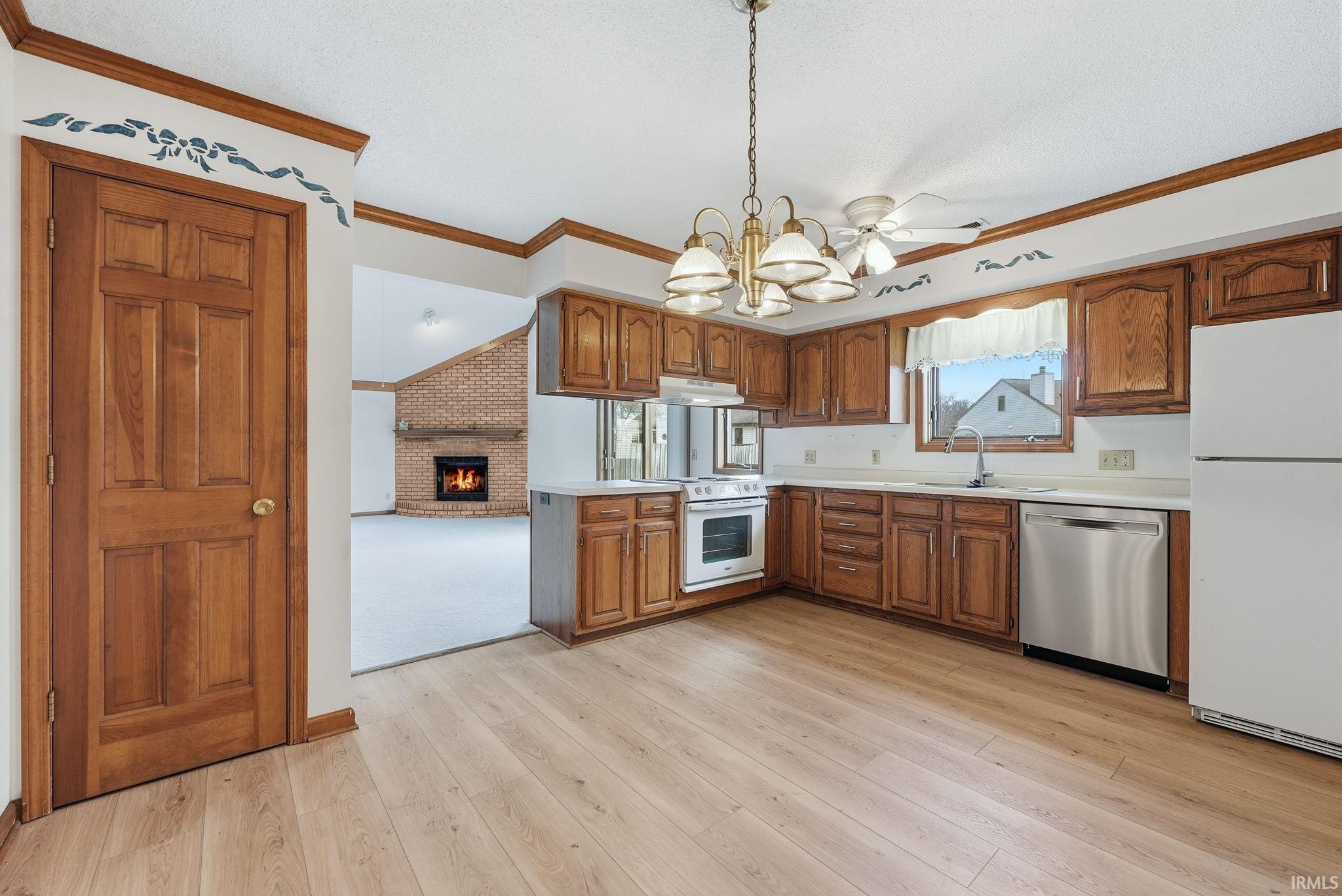Kitchen featuring white appliances, wood finish cabinetry, light countertops, ornamental molding, and suspended lighting