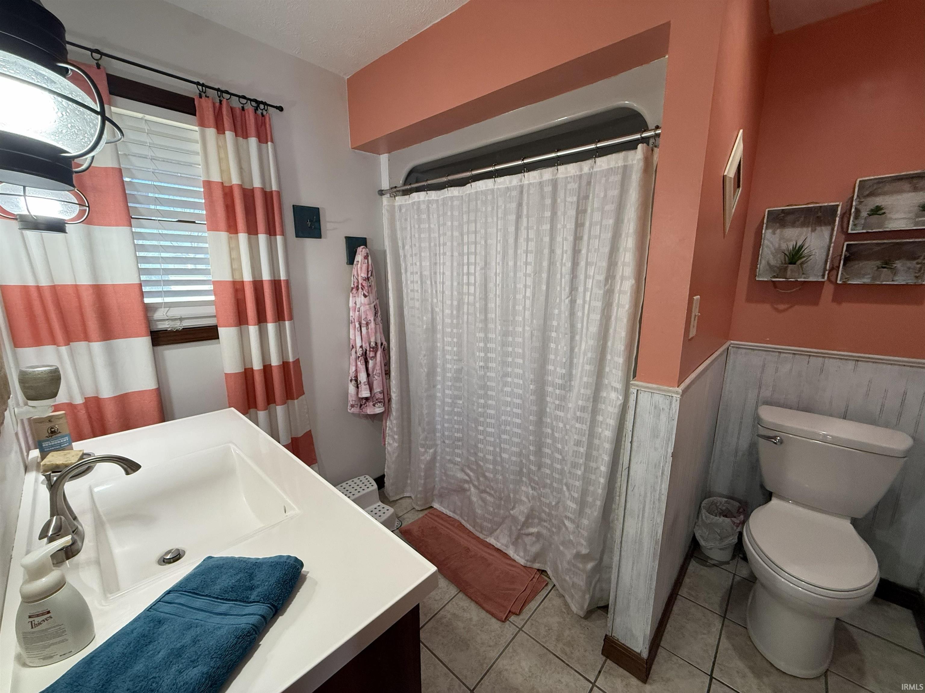Bathroom featuring vanity, a shower with curtain, a wainscoted wall, and light tile patterned floors
