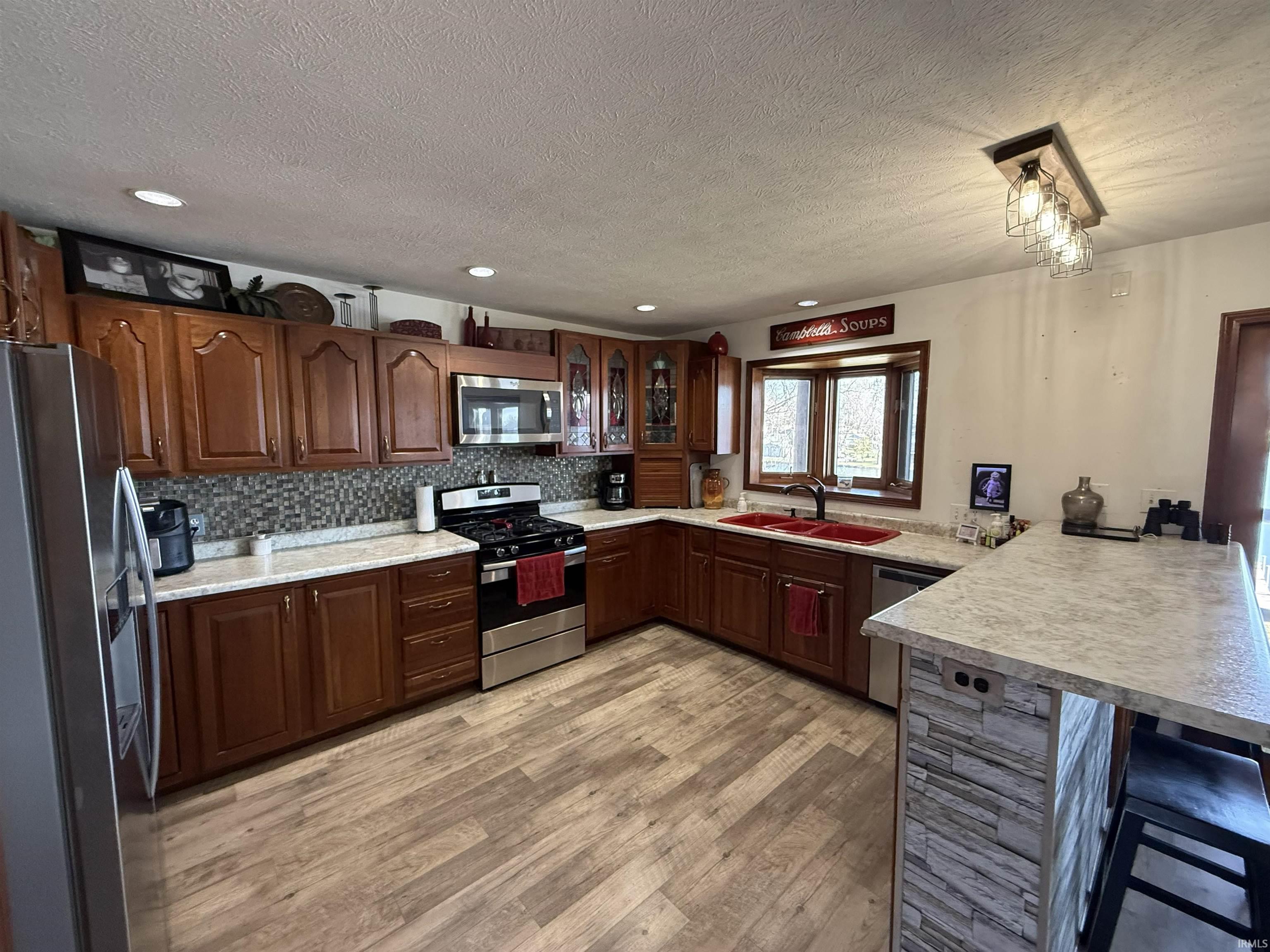 Kitchen with stainless steel appliances, a peninsula, light countertops, a kitchen breakfast bar, and glass fronted cabinets