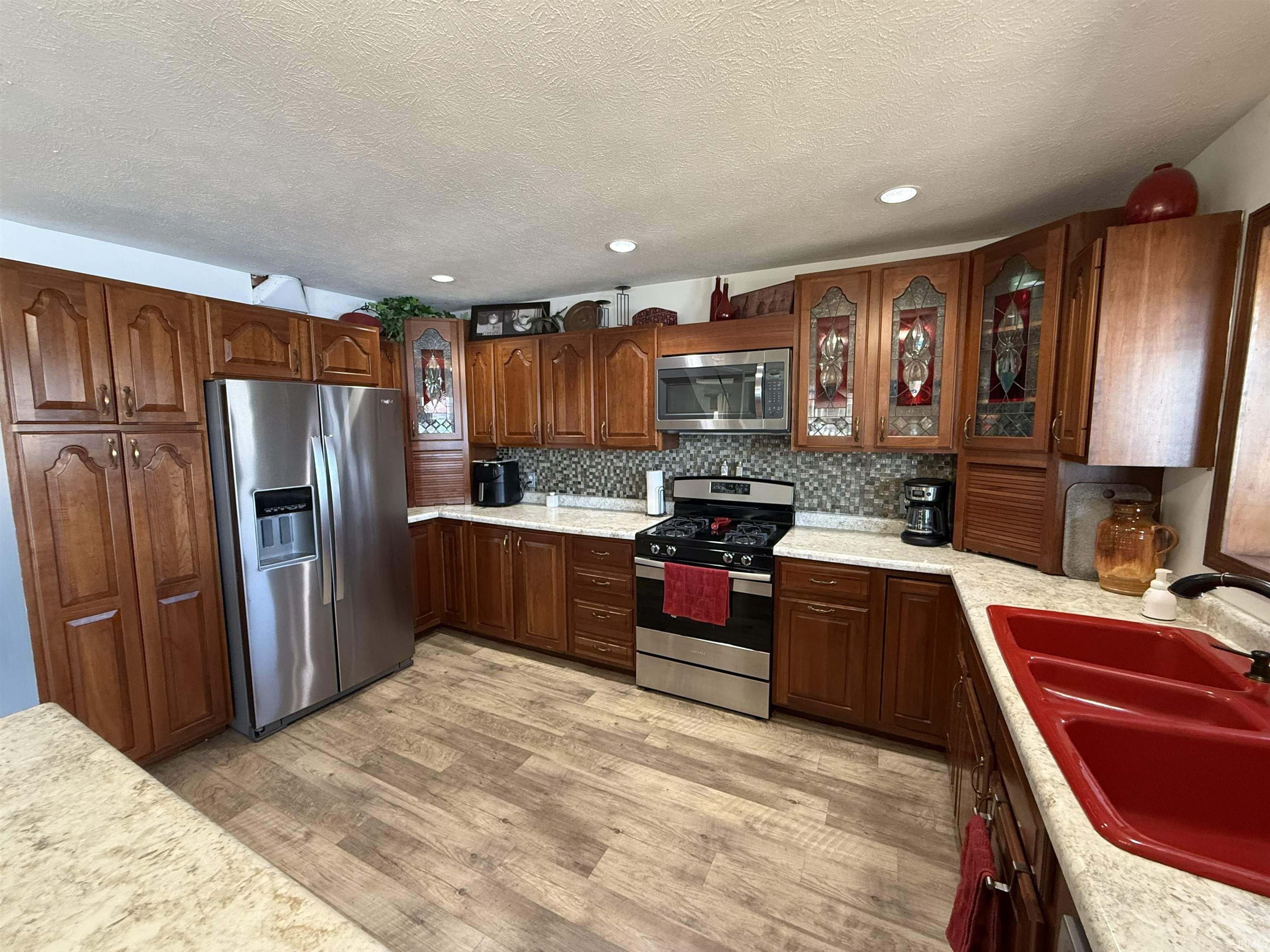 Kitchen with glass fronted cabinets, stainless steel appliances, light wood-style floors, a textured ceiling, and tasteful backsplash