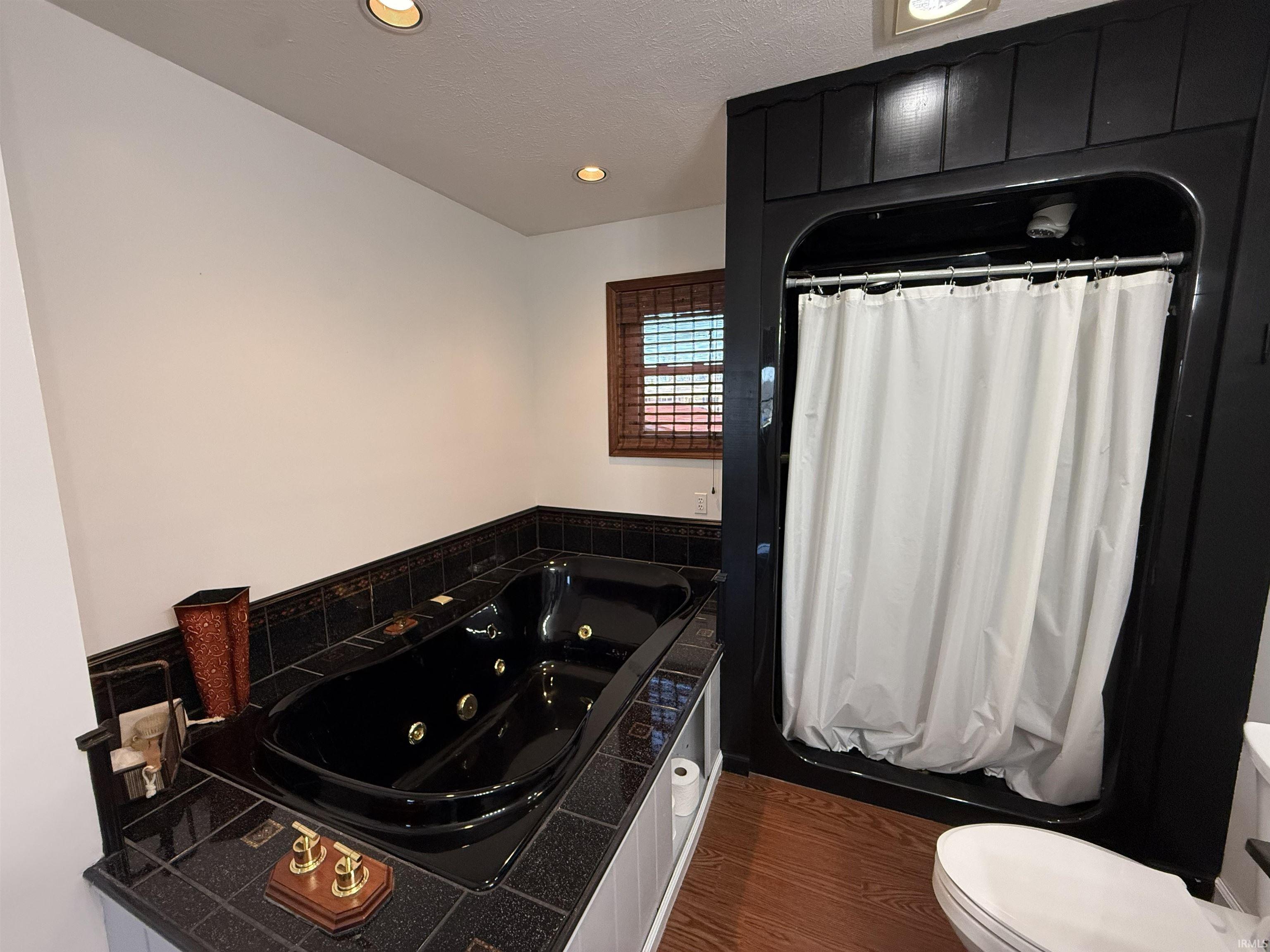 Full bathroom with a tub with jets, dark wood-type flooring, recessed lighting, curtained shower, and a textured ceiling