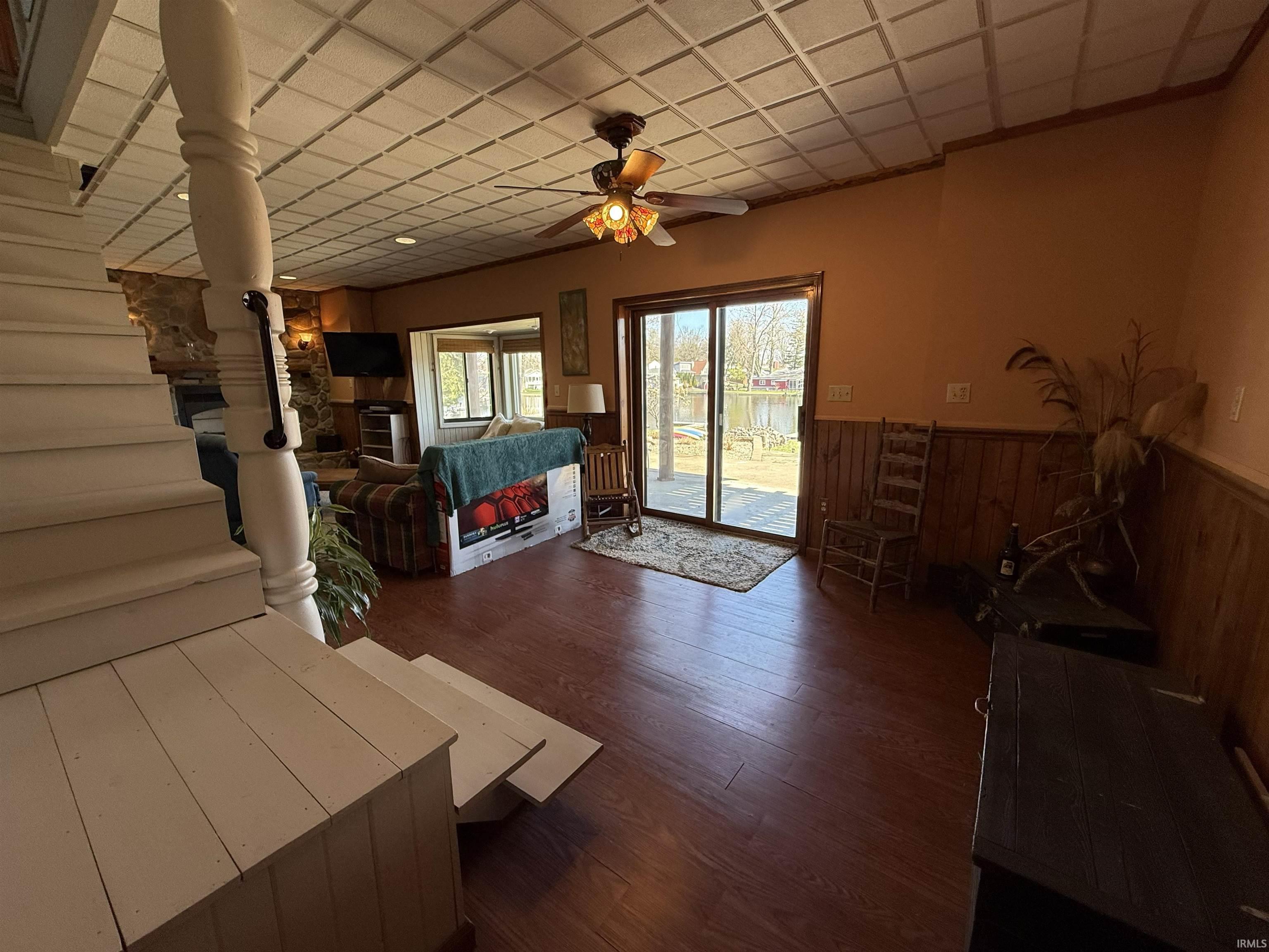 Living area featuring a wainscoted wall, wood walls, ceiling fan, dark wood finished floors, and a paneled ceiling