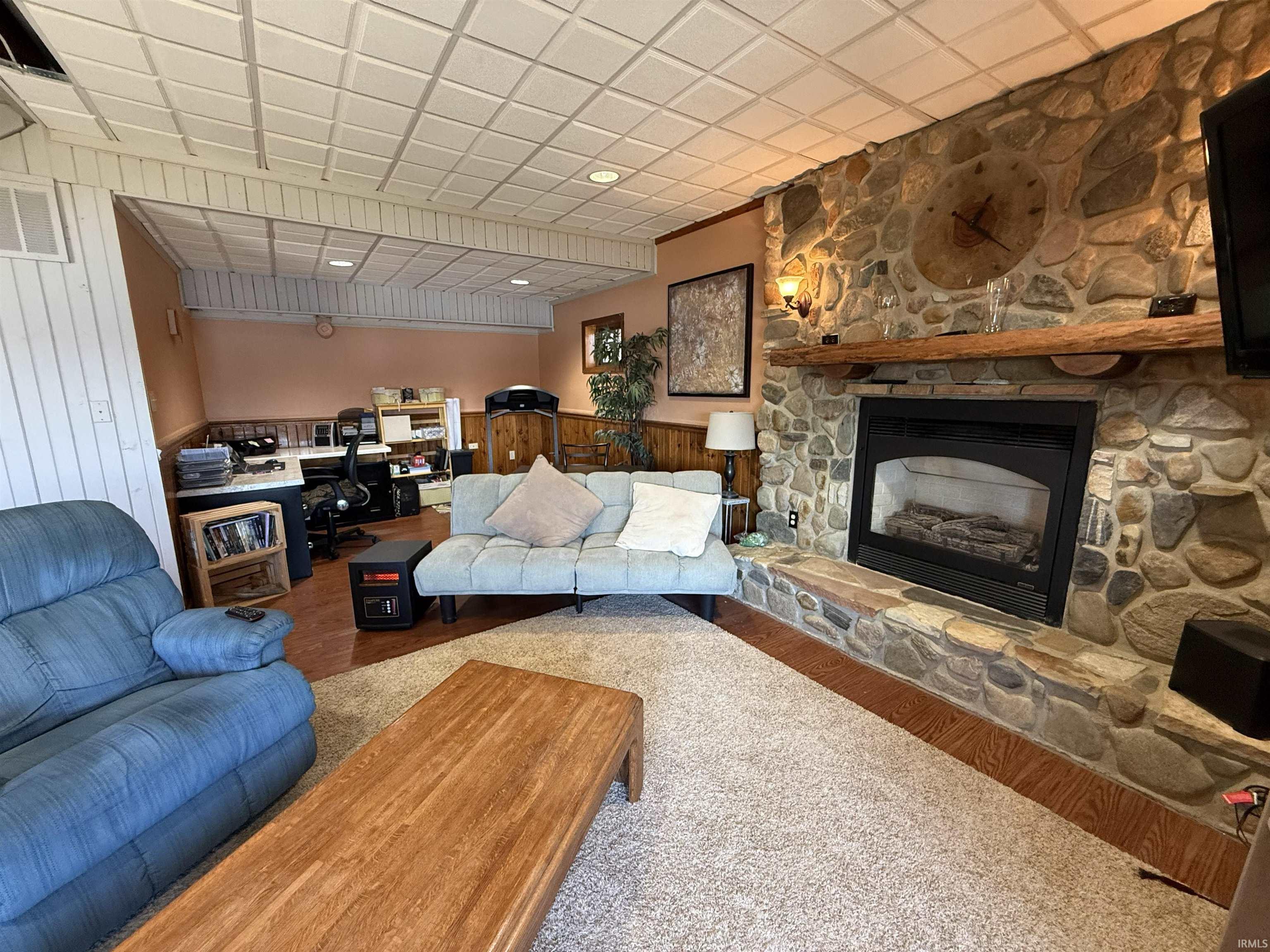 Living room featuring a stone fireplace, wood finished floors, a drop ceiling, and an office area