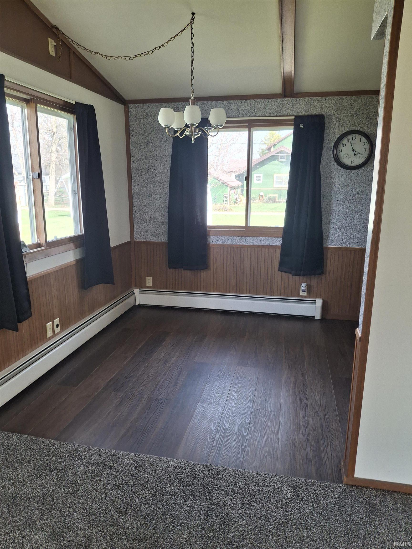 Unfurnished dining area with a wainscoted wall, wallpapered walls, hanging lights, a baseboard radiator, and lofted ceiling with beams