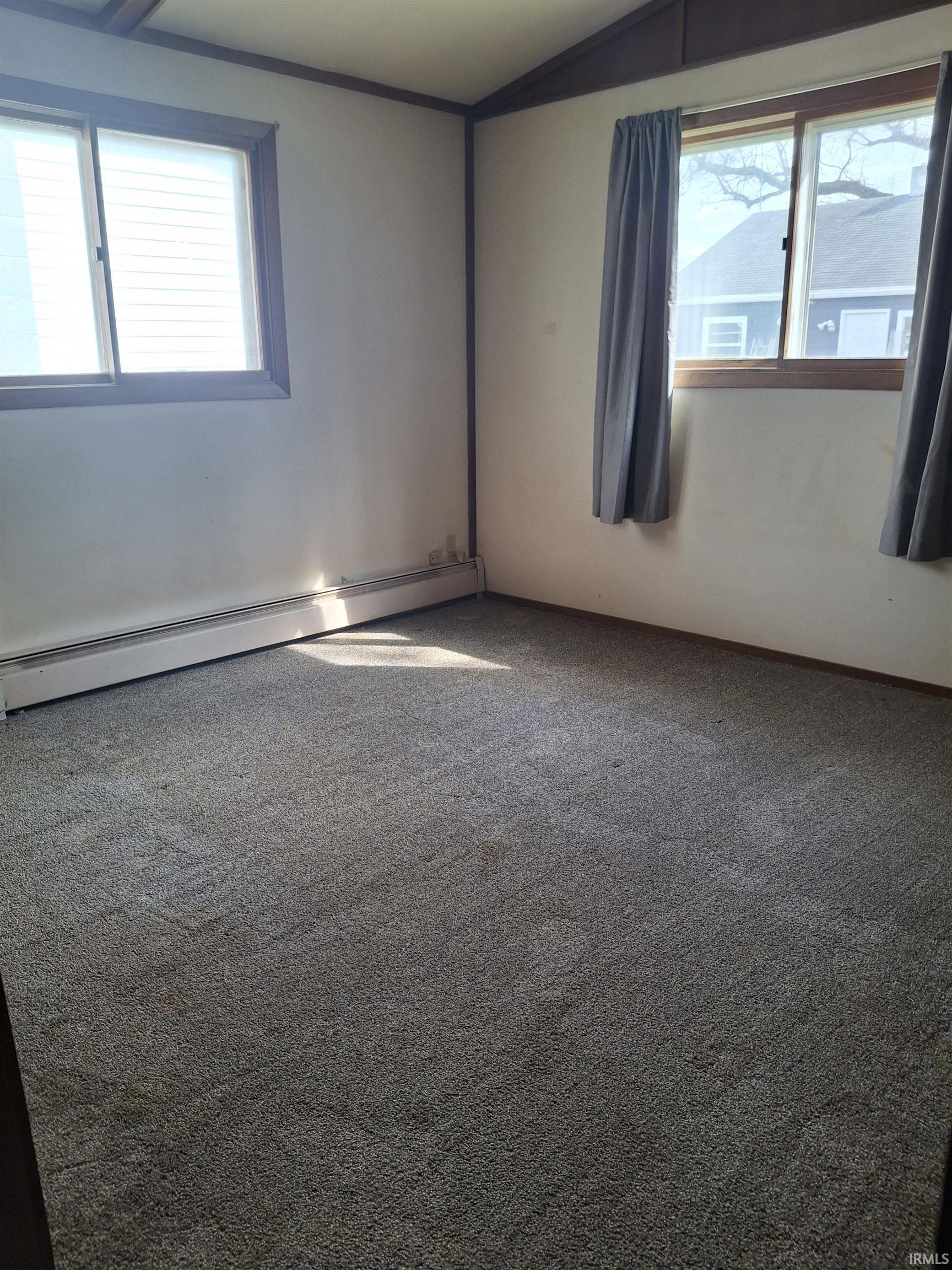 Carpeted spare room with a baseboard heating unit and vaulted ceiling