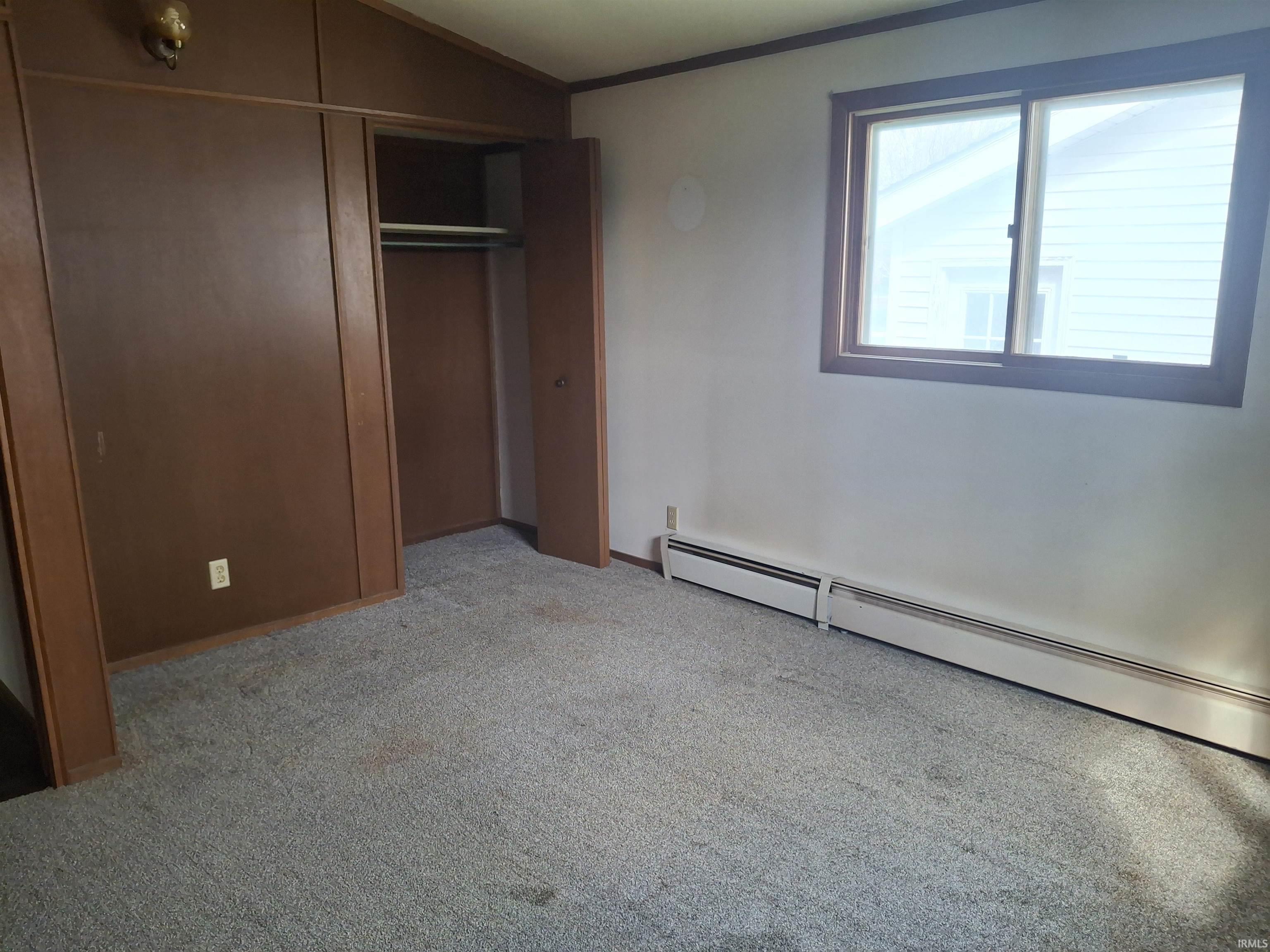 Unfurnished bedroom with a baseboard radiator, light colored carpet, a closet, lofted ceiling, and crown molding