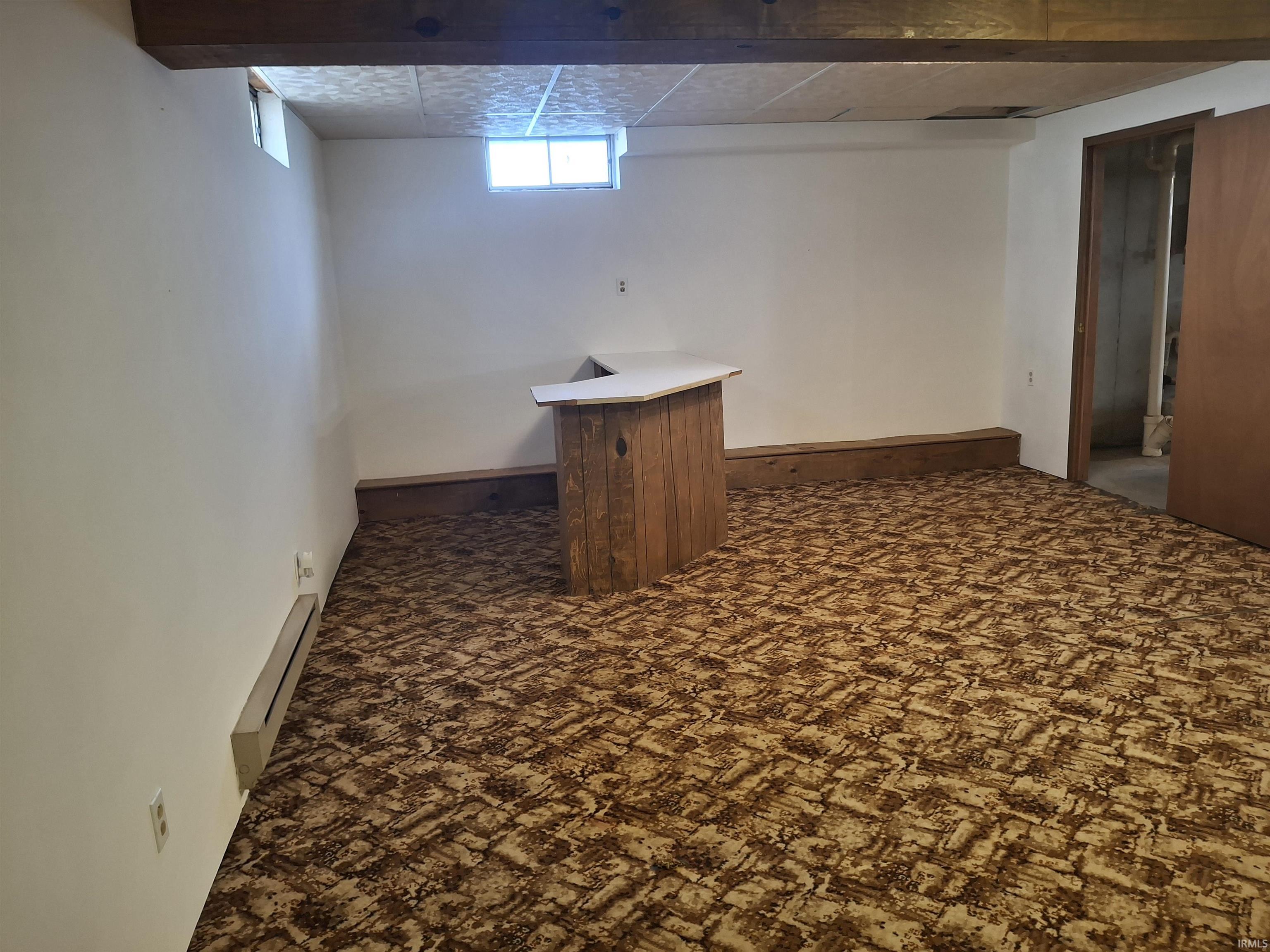 Basement featuring baseboard heating, a bar, and dark colored carpet