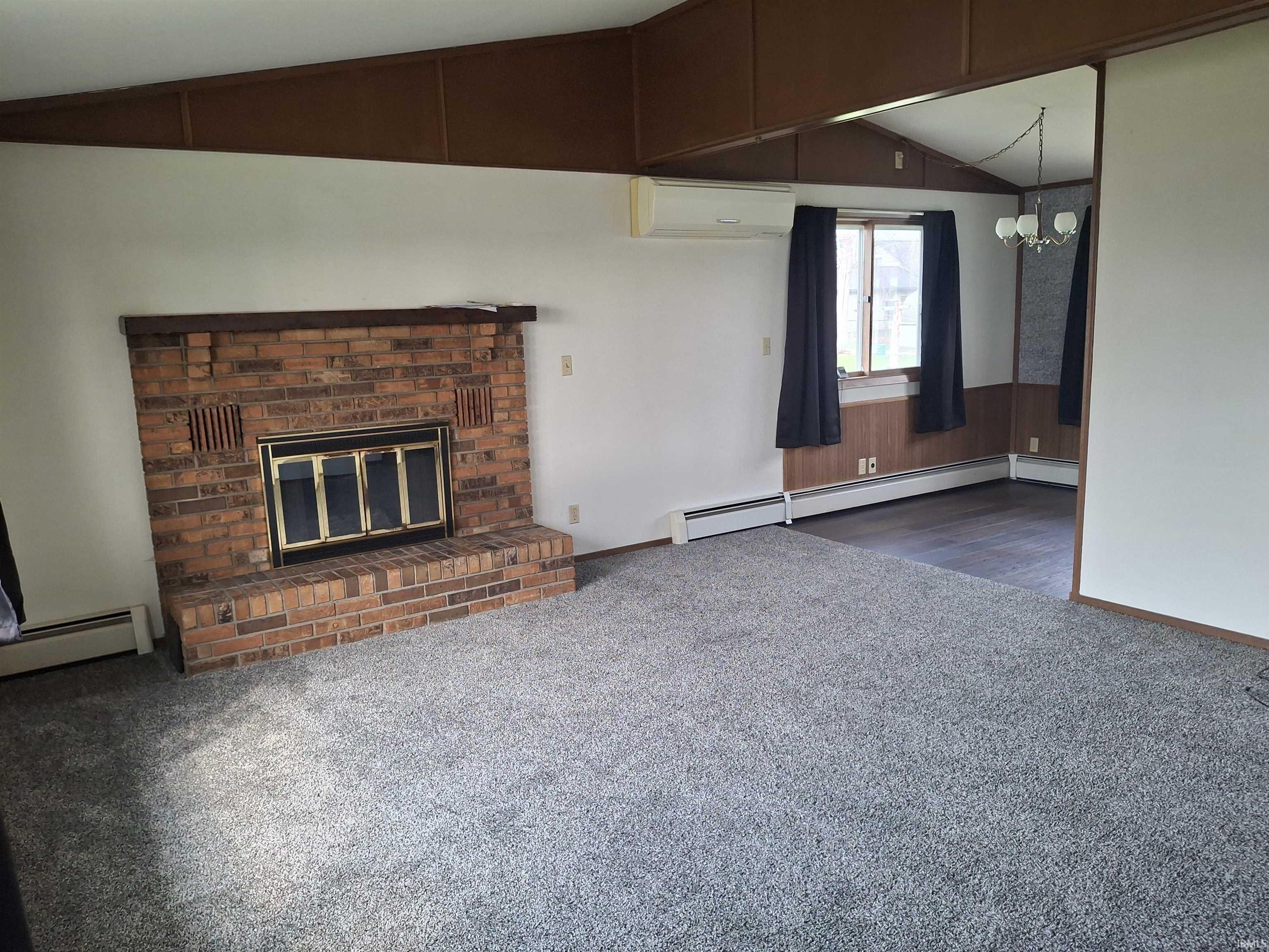 Unfurnished living room featuring vaulted ceiling, dark carpet, hanging lights, a fireplace, and baseboard heating