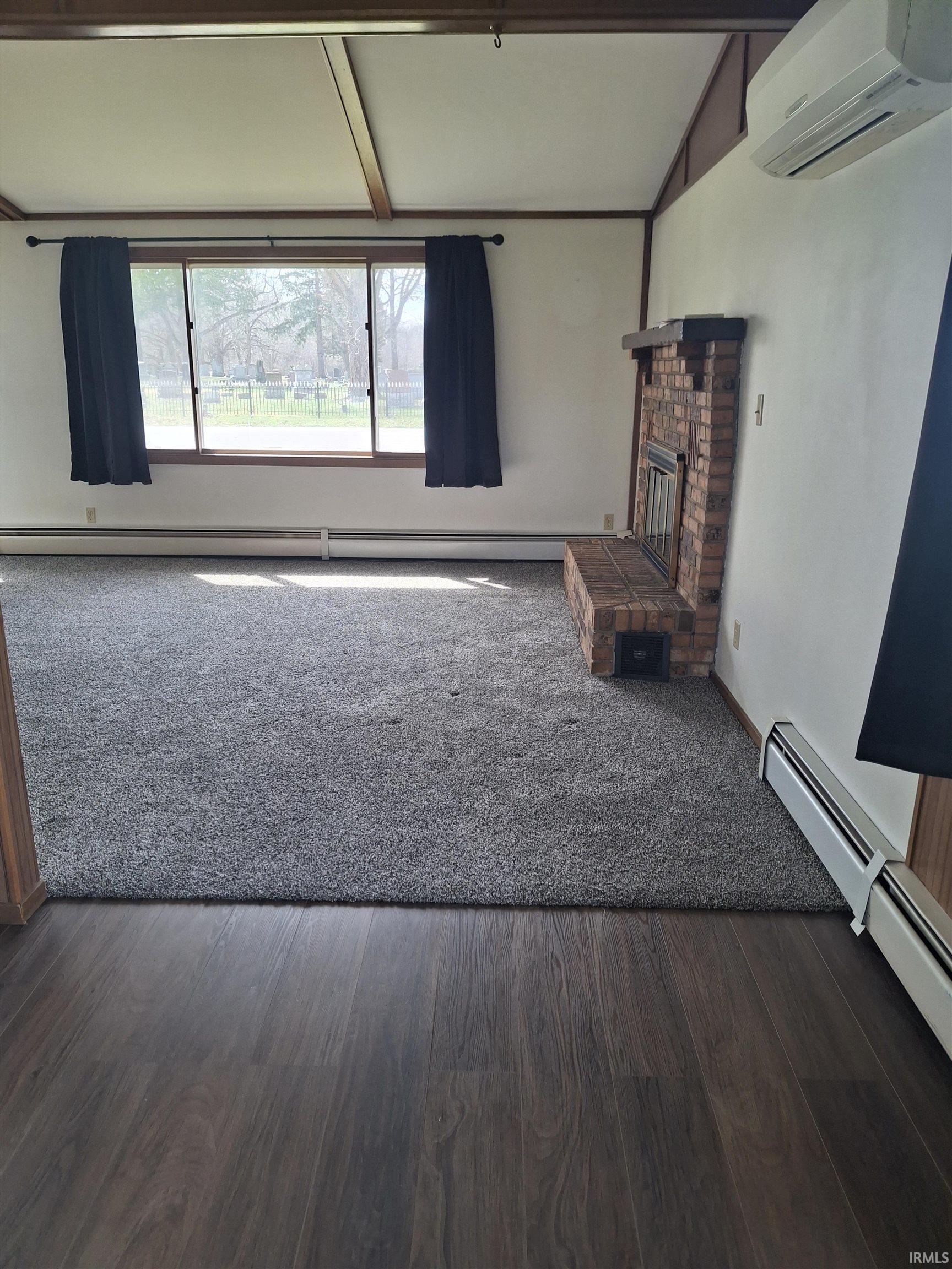 Unfurnished living room with a brick fireplace, a baseboard heating unit, dark wood-style floors, and beamed ceiling