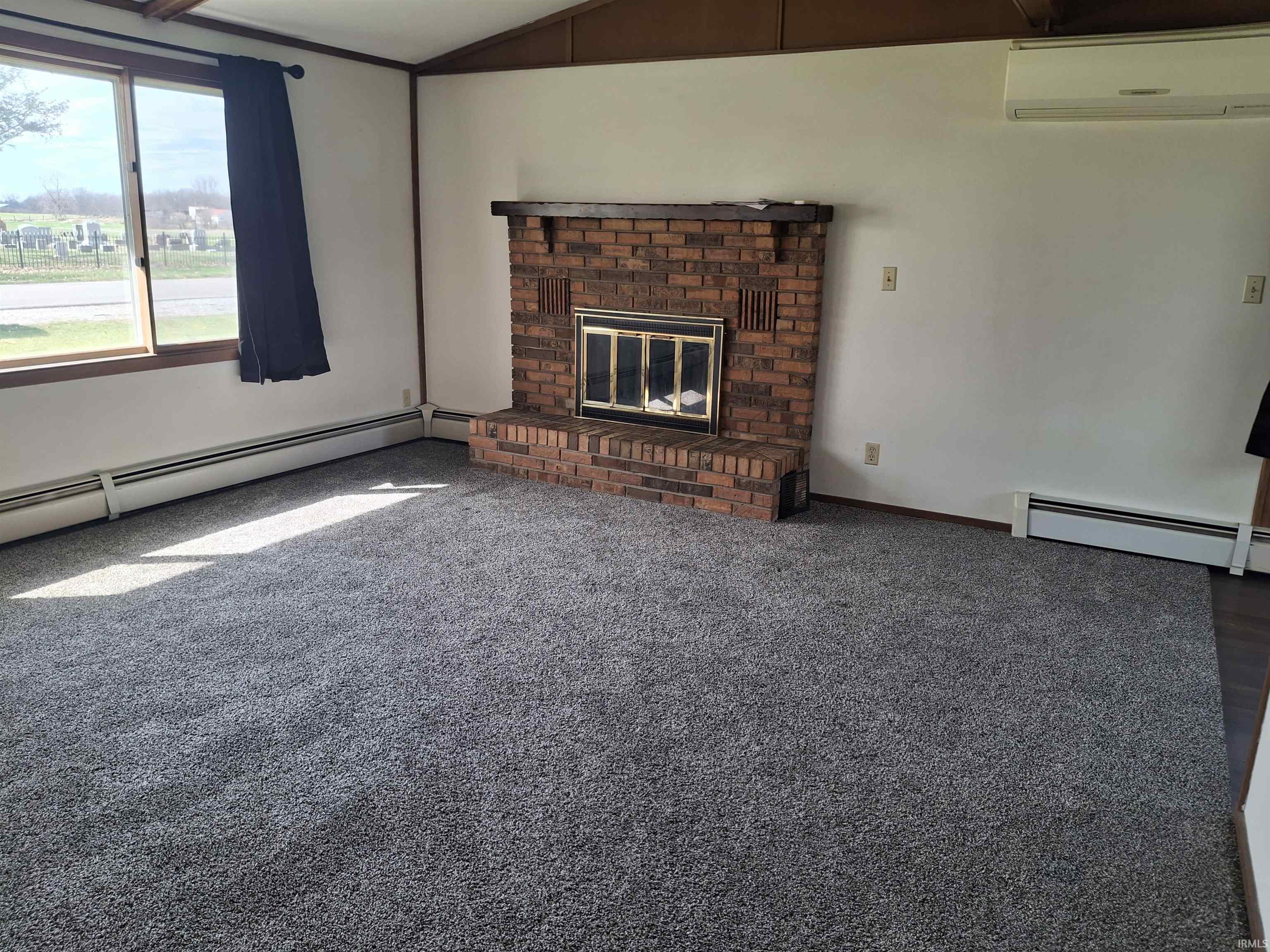 Unfurnished living room featuring lofted ceiling, a brick fireplace, a baseboard heating unit, and carpet flooring