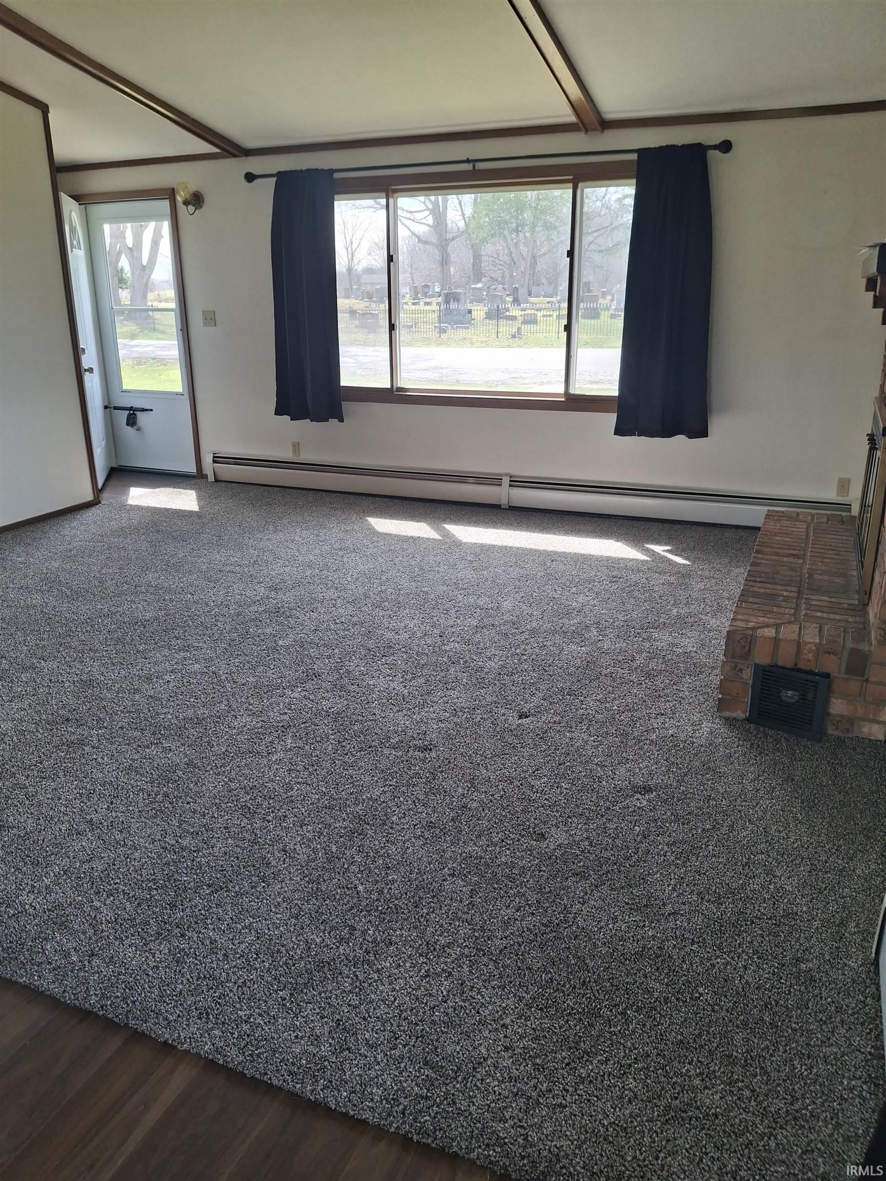 Unfurnished living room with a baseboard heating unit, healthy amount of natural light, and dark colored carpet