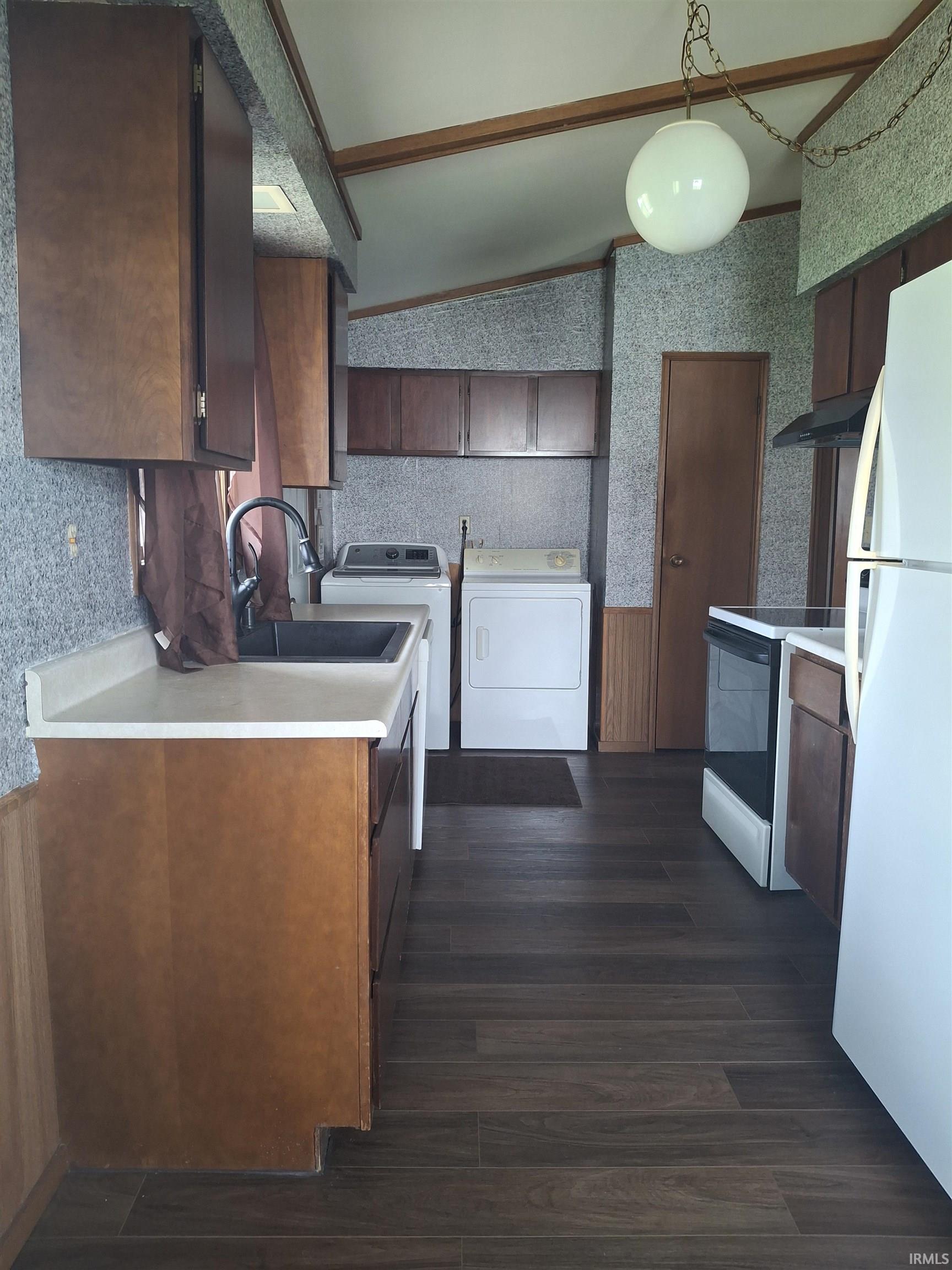 Kitchen with vaulted ceiling, freestanding refrigerator, light countertops, range with electric cooktop, and wallpapered walls