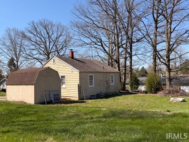 View of side of property with a storage unit, a lawn, and a chimney