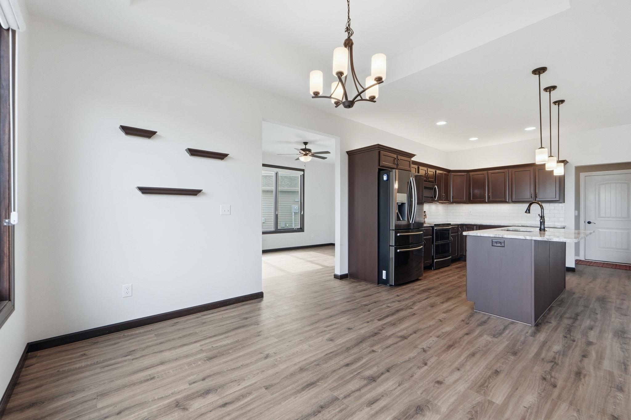 Kitchen with dark wood finish cabinets, hanging lights, decorative backsplash, stainless steel appliances, and a kitchen island with sink