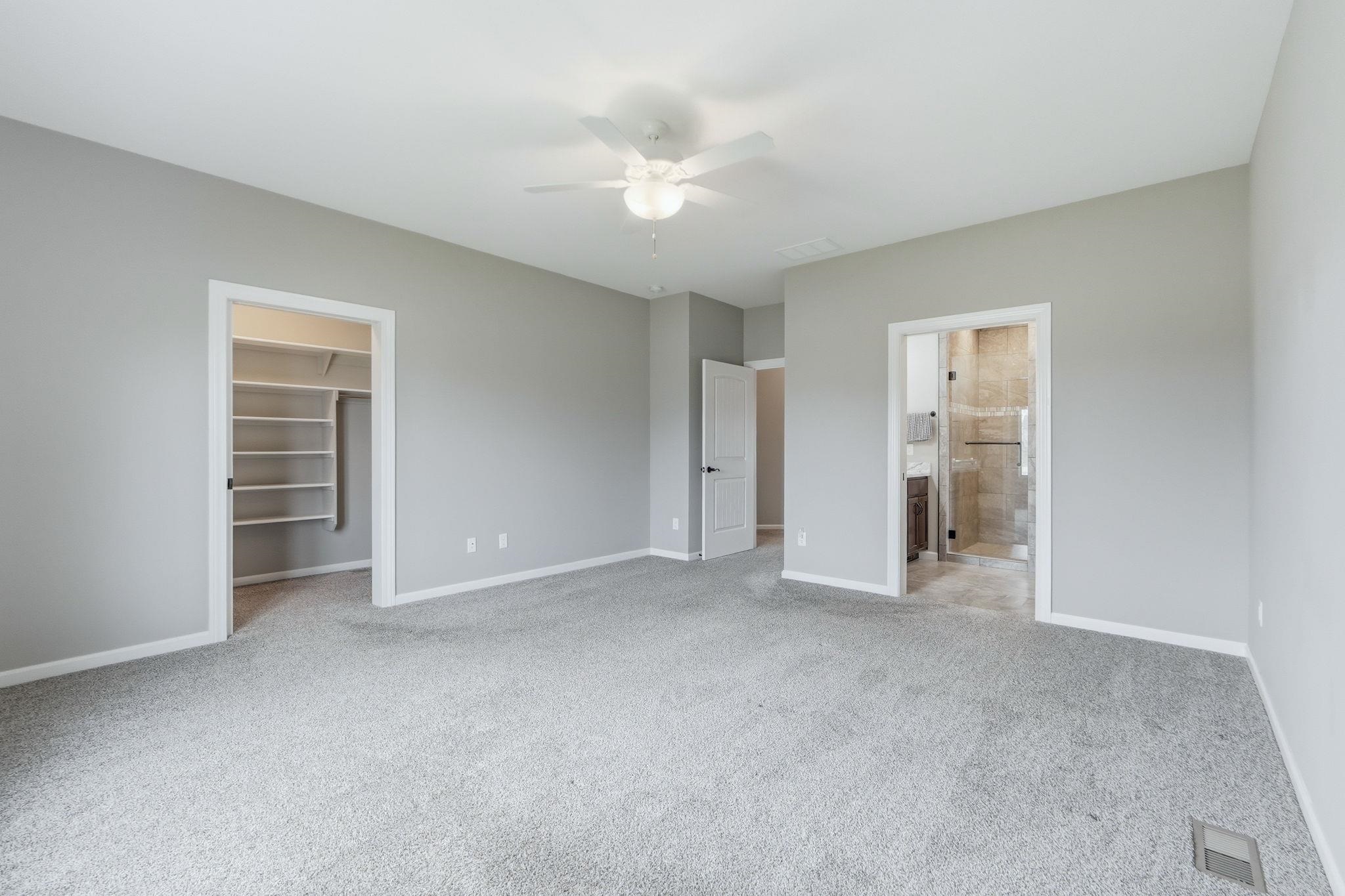 Unfurnished bedroom with a spacious closet, light colored carpet, and a ceiling fan