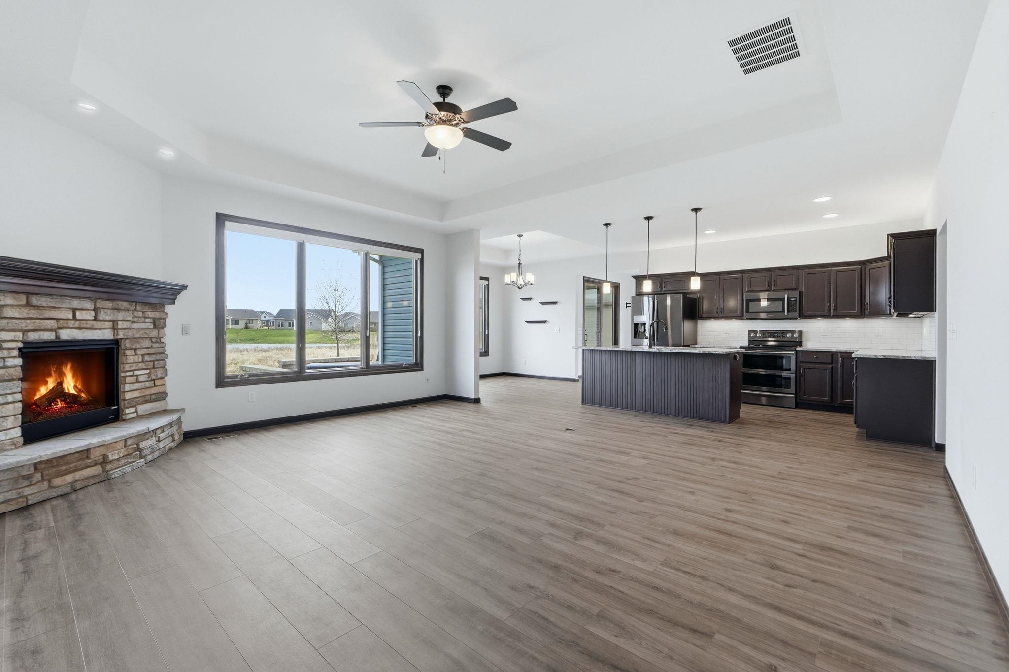 Unfurnished living room with hanging lights, a tray ceiling, ceiling fan, a fireplace, and light wood-style flooring