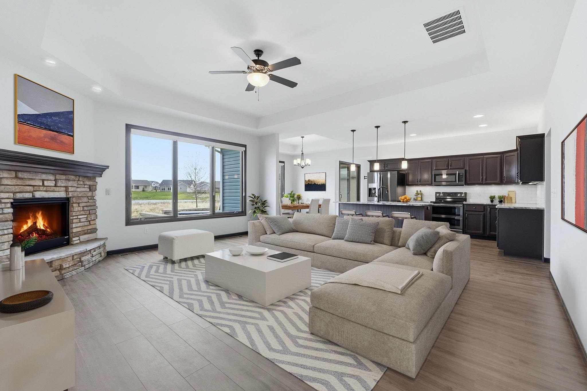 Living room featuring a tray ceiling, light wood-type flooring, a chandelier, ceiling fan, and a fireplace