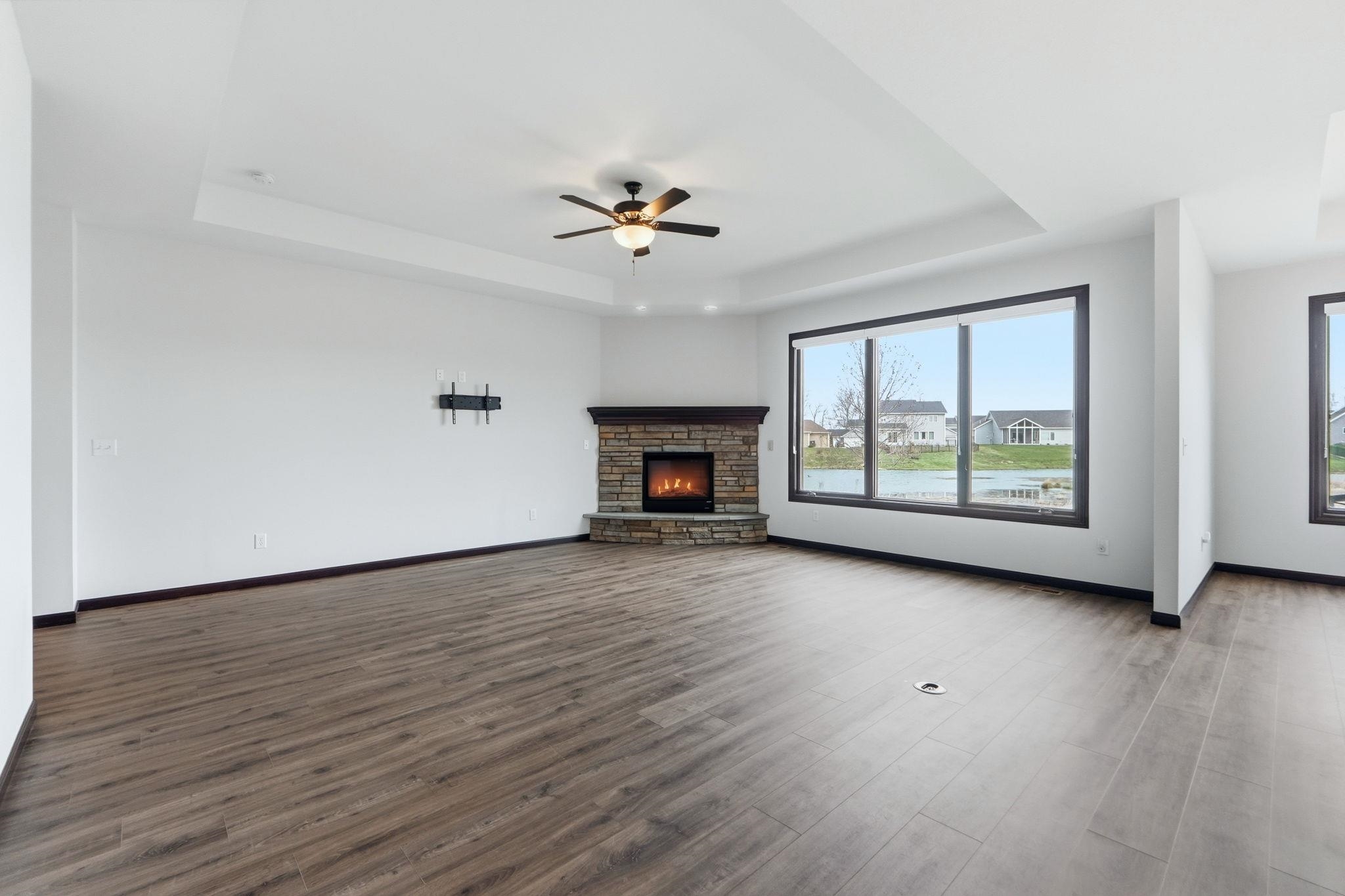 Unfurnished living room featuring dark wood-type flooring, a raised ceiling, a ceiling fan, and a fireplace