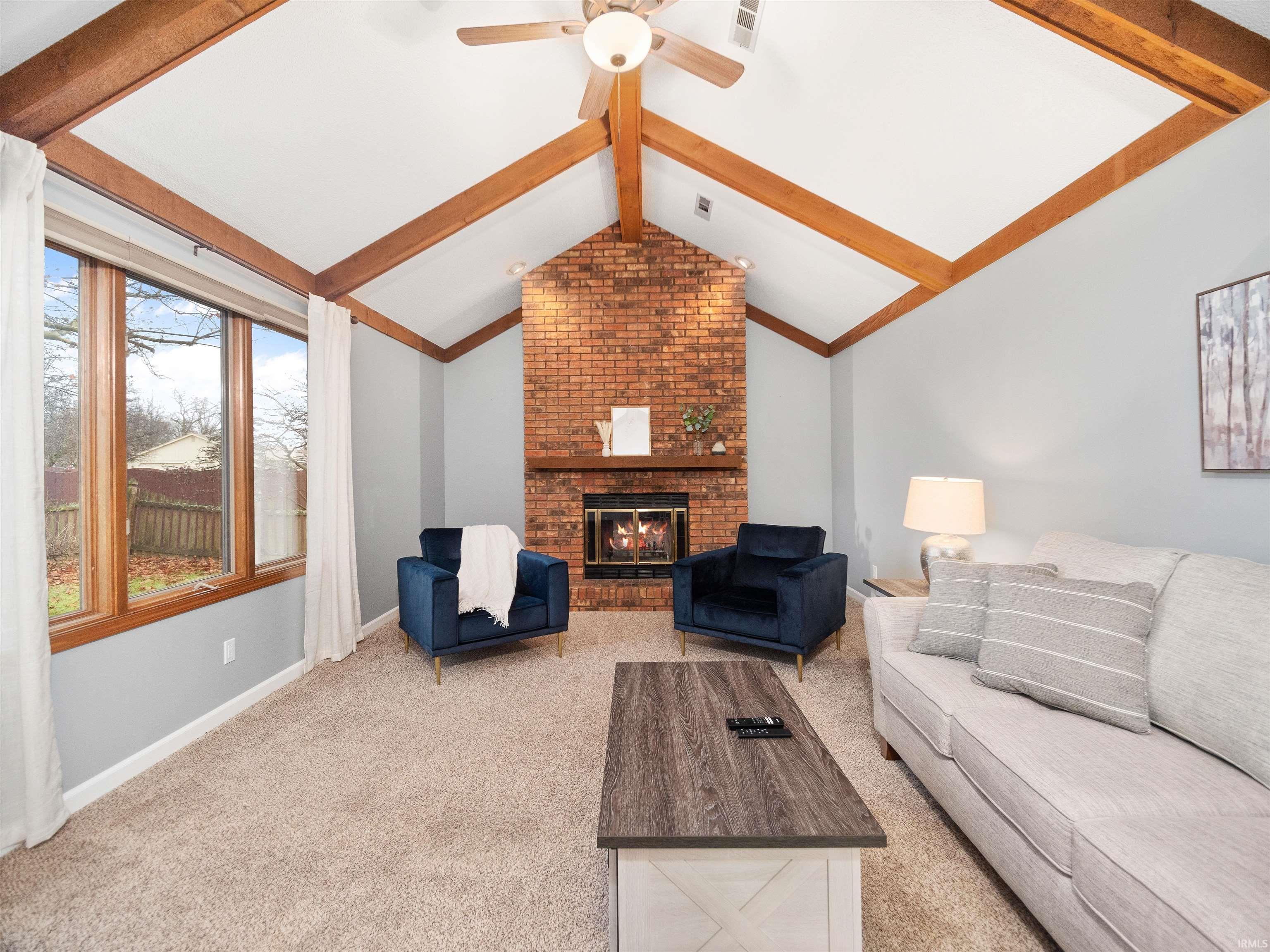 Living room with beam ceiling, a brick fireplace, light carpet, and ceiling fan