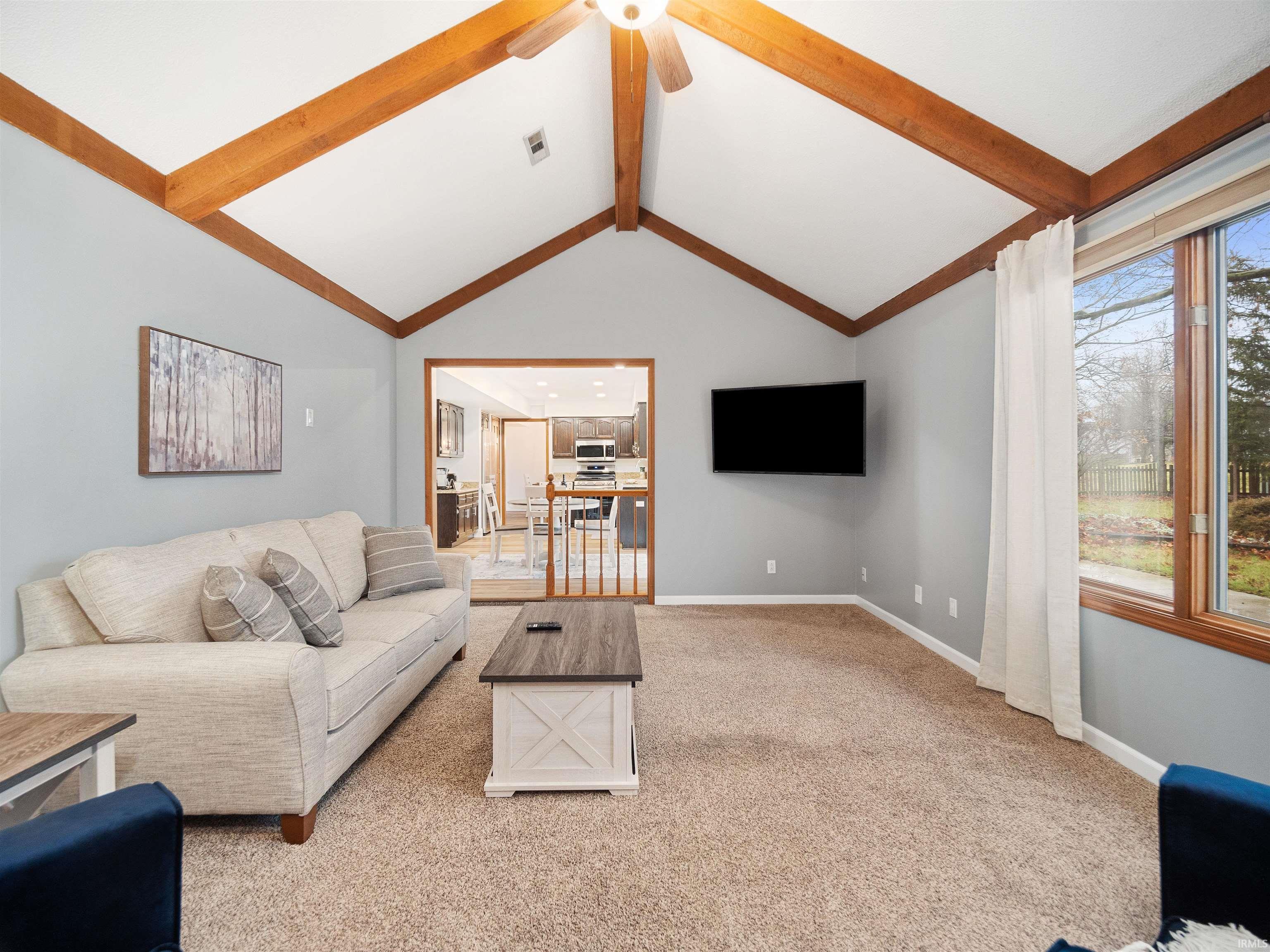 Living area featuring light colored carpet, a ceiling fan, and beam ceiling