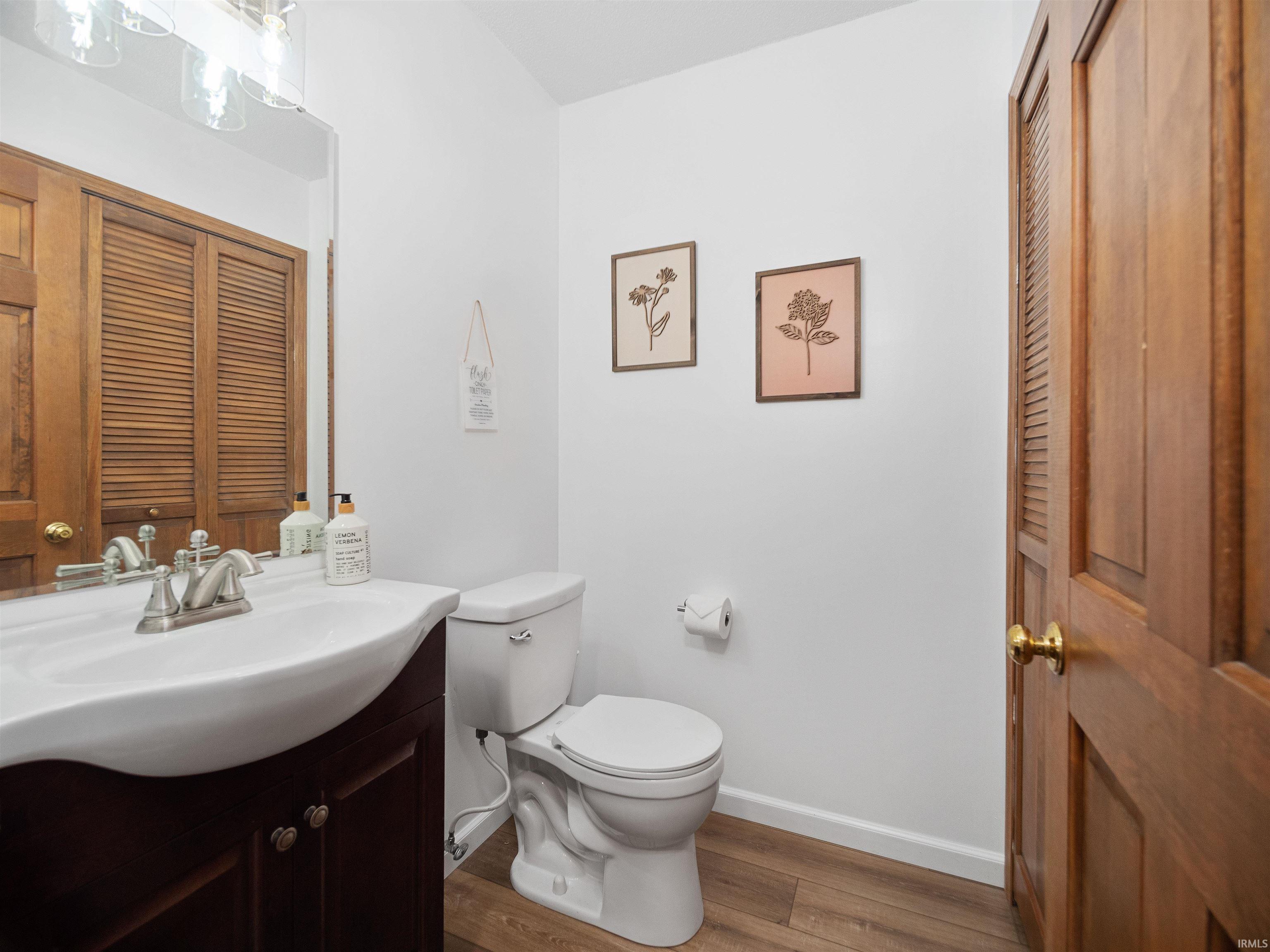 Half bathroom with vanity, a closet, and dark wood-type flooring