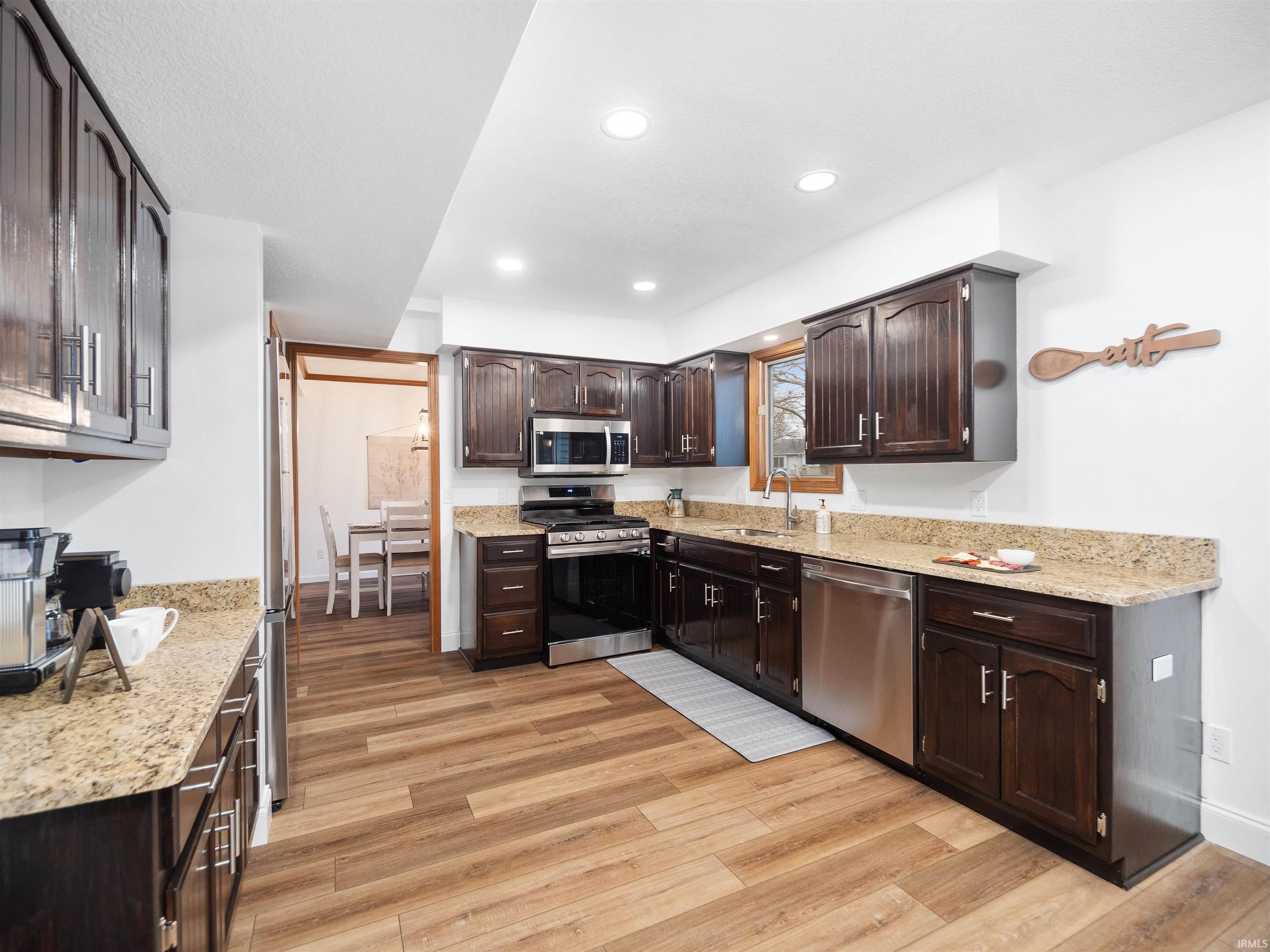 Kitchen with stainless steel appliances, light stone countertops, dark wood finish cabinetry, light wood-style flooring, and recessed lighting