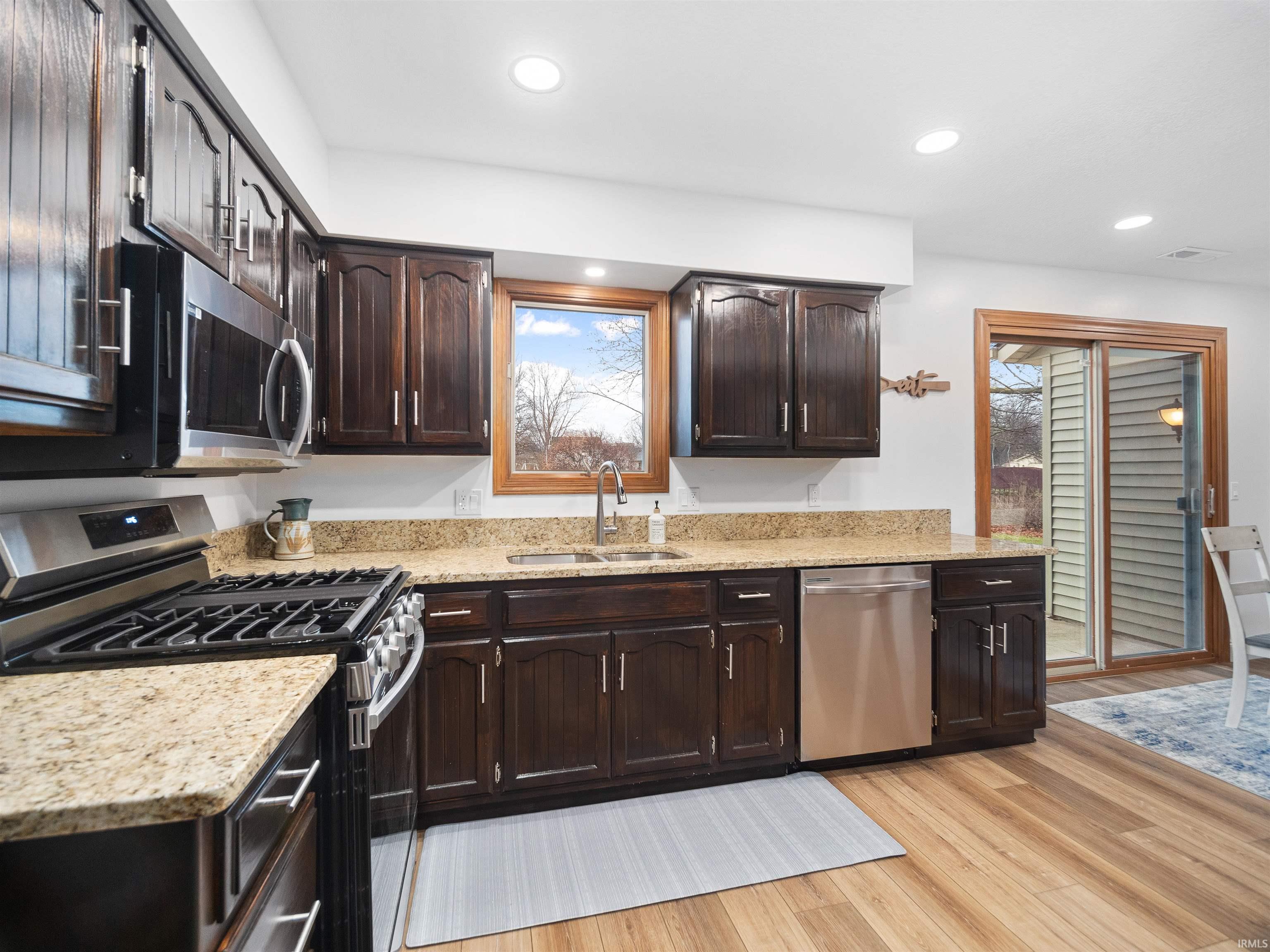 Kitchen featuring stainless steel appliances, light stone counters, dark wood finish cabinets, and recessed lighting