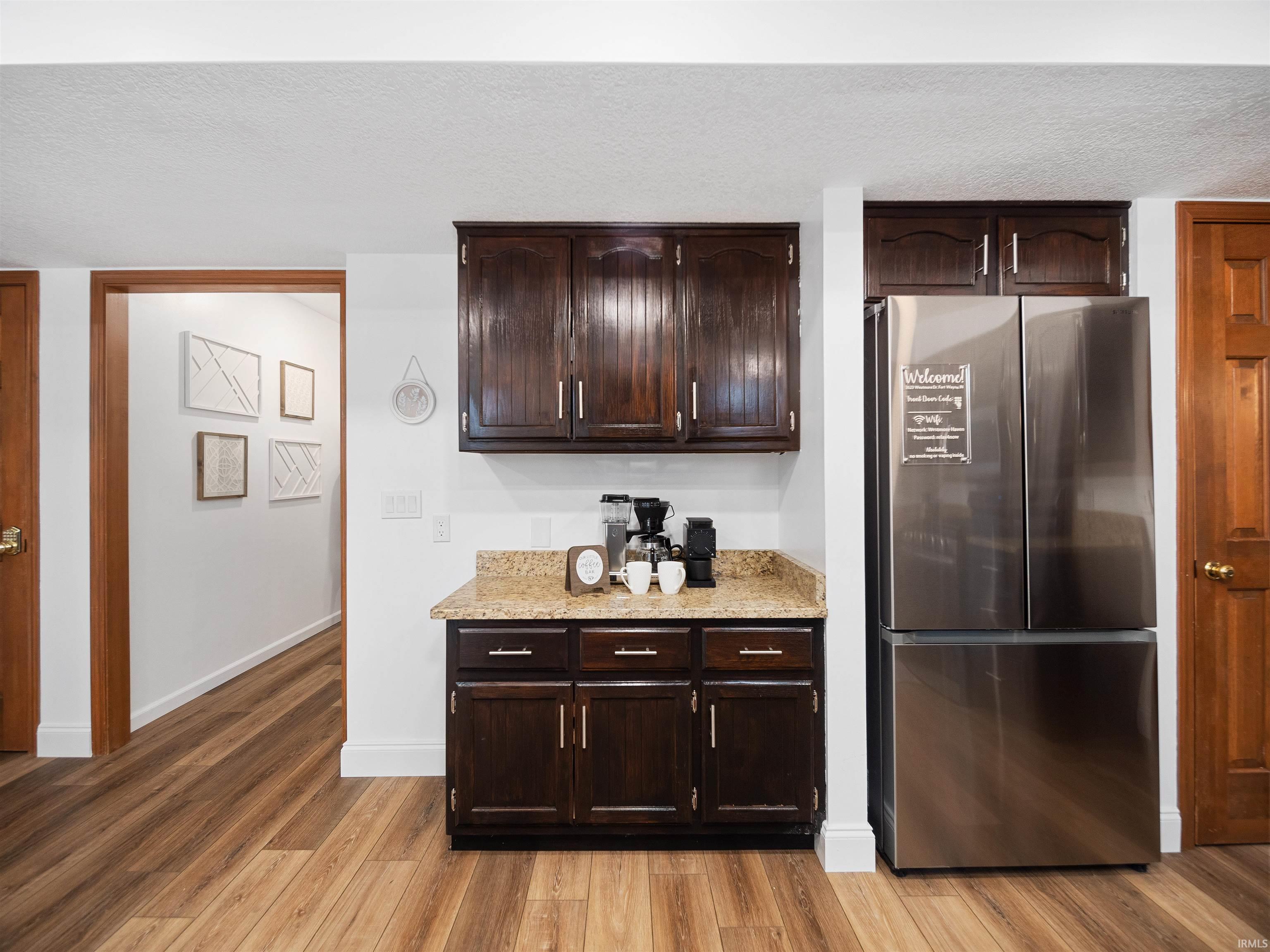 Bar area featuring dark wood finish cabinetry, freestanding refrigerator, a textured ceiling, light wood-style floors, and light stone countertops