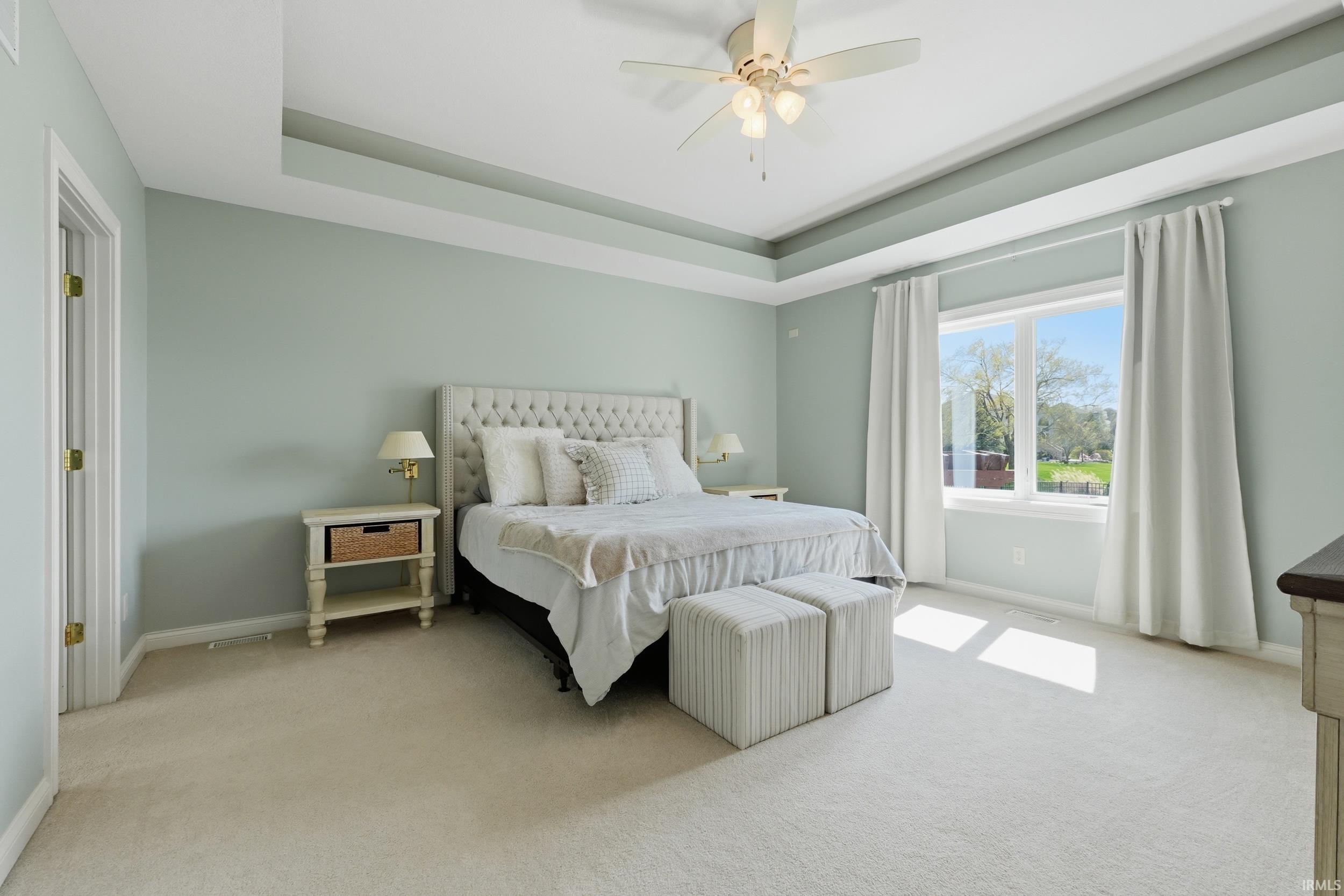 Bedroom featuring a tray ceiling, light carpet, and ceiling fan