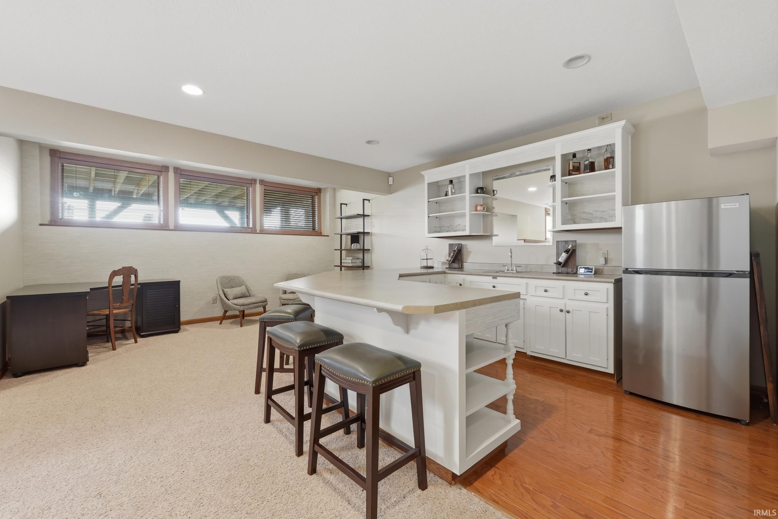 Kitchen featuring open shelves, freestanding refrigerator, white cabinetry, a breakfast bar area, and light countertops