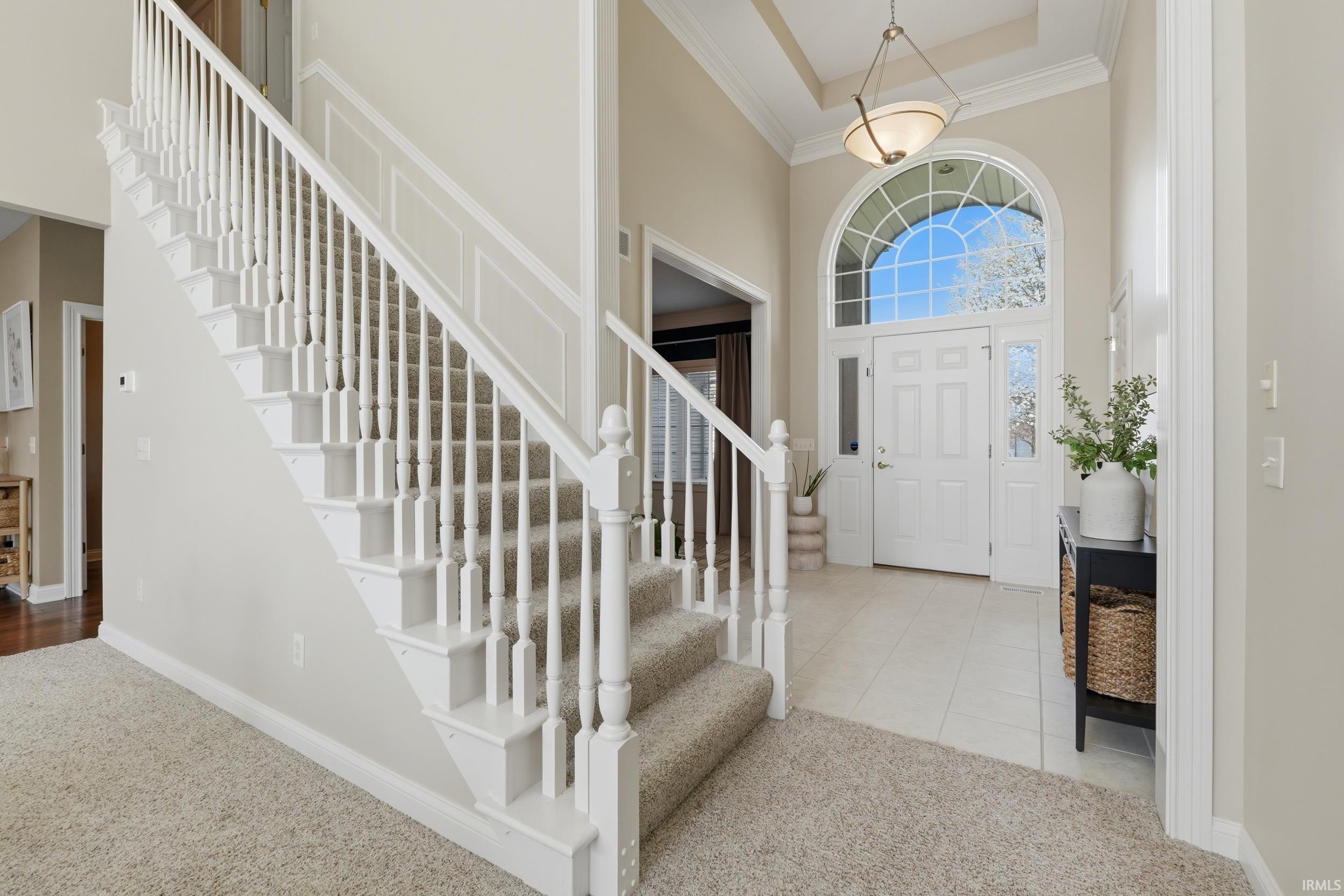 Foyer with a high ceiling, carpet, ornamental molding, and tile patterned floors