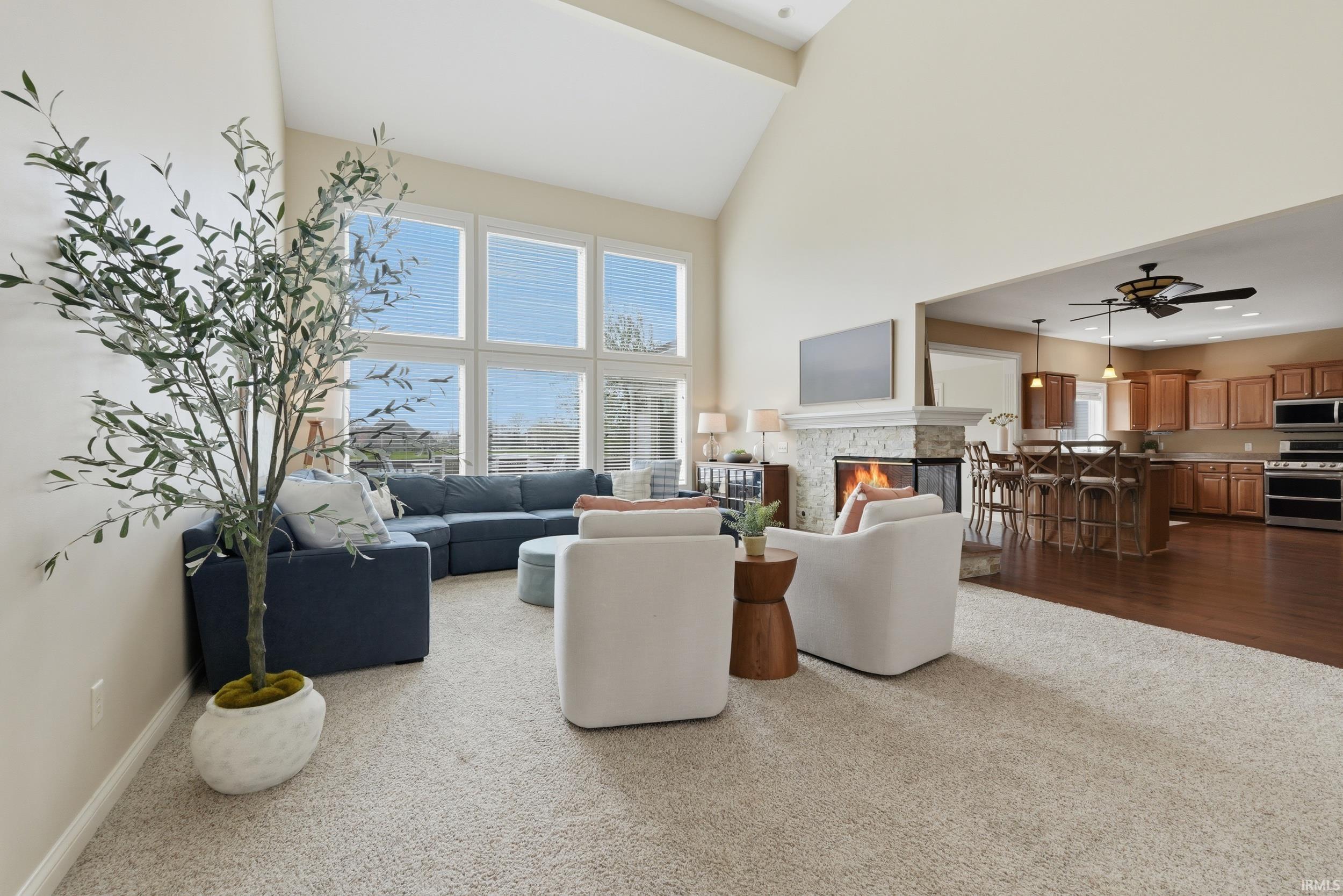 Living room with dark colored carpet, a fireplace, a high ceiling, and a ceiling fan
