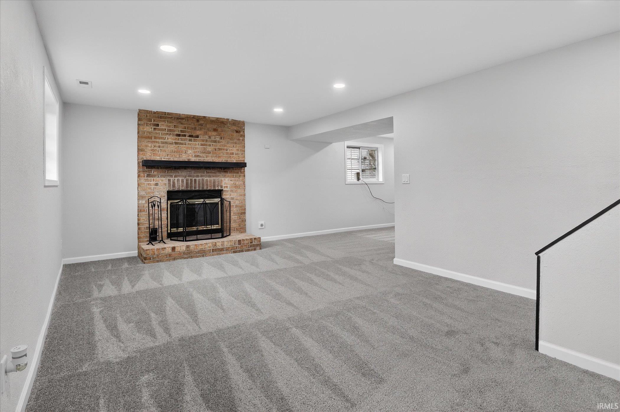 Unfurnished living room featuring a brick fireplace, recessed lighting, and light carpet
