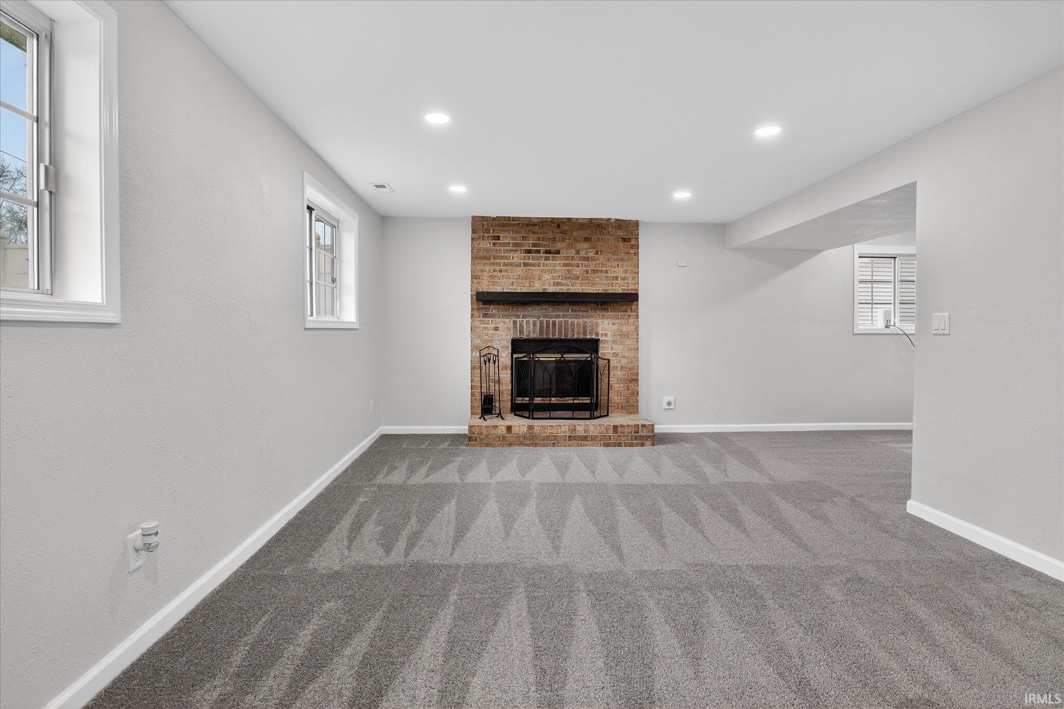 Unfurnished living room with a brick fireplace, recessed lighting, plenty of natural light, and light carpet