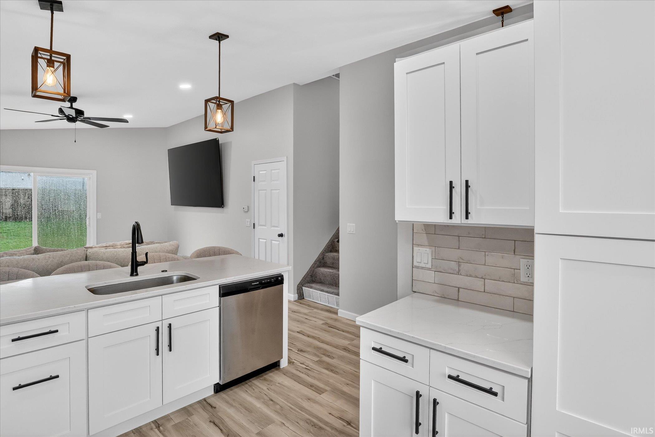 Kitchen featuring white cabinetry, dishwasher, open floor plan, light wood finished floors, and a ceiling fan