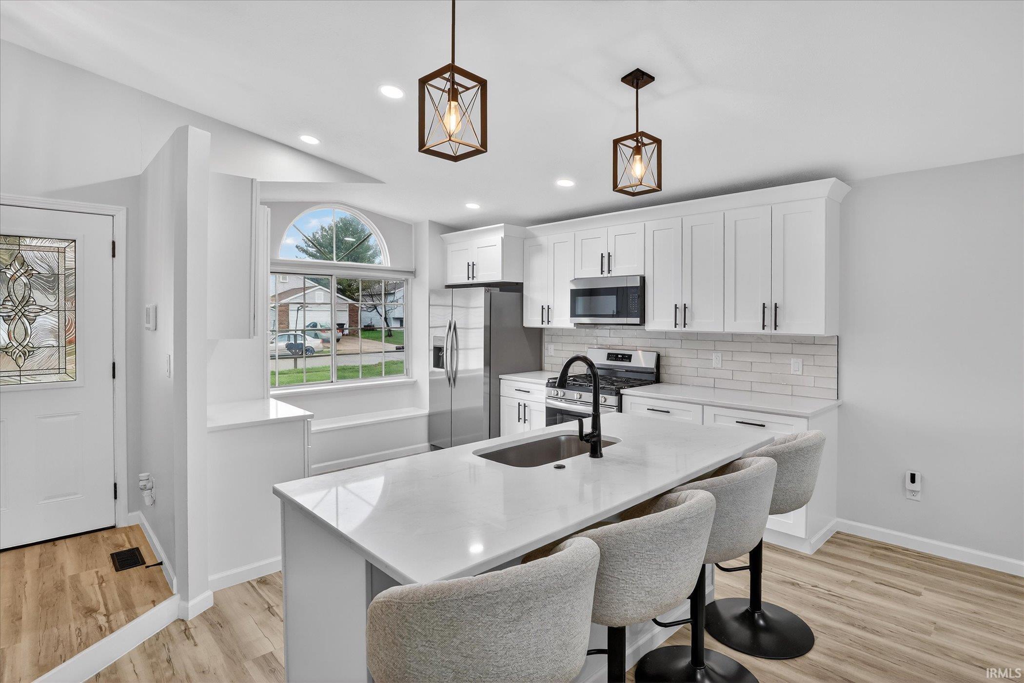 Kitchen with stainless steel appliances, white cabinetry, light stone countertops, light wood-style flooring, and a breakfast bar