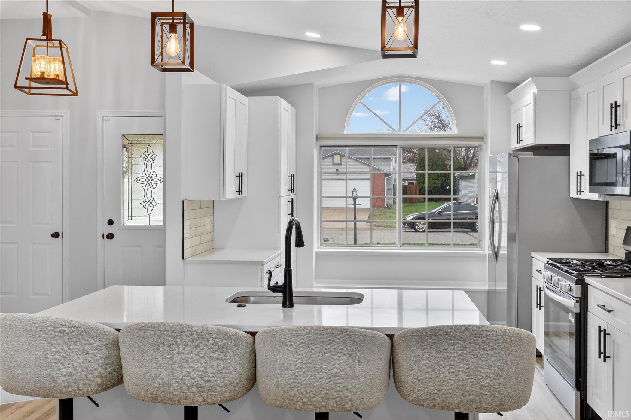 Kitchen featuring stainless steel appliances, light stone countertops, decorative backsplash, and white cabinets