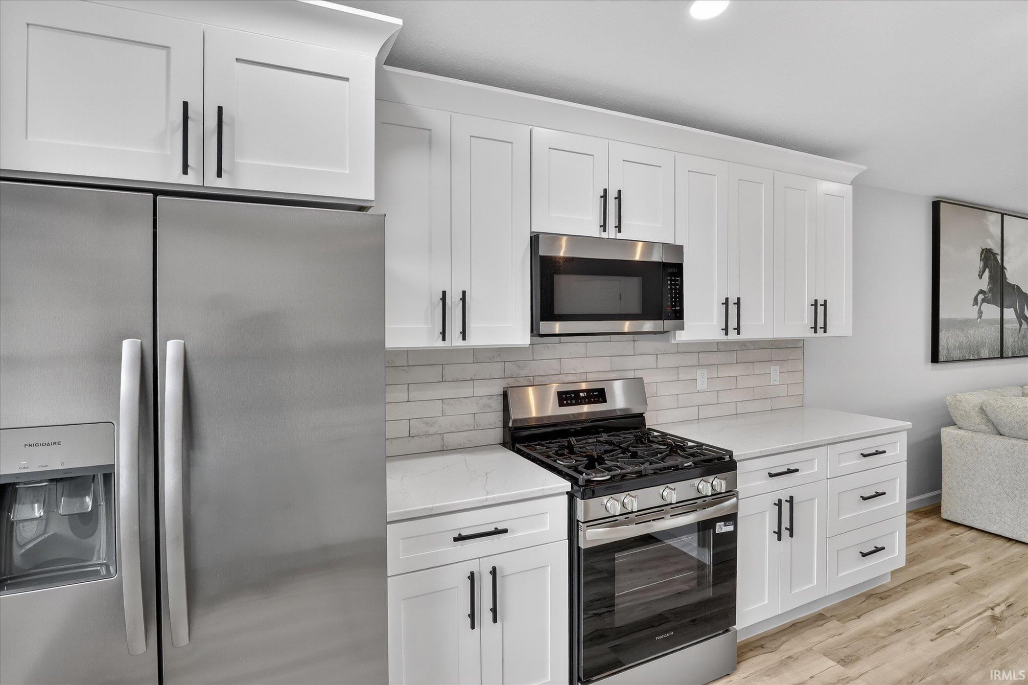 Kitchen featuring stainless steel appliances, white cabinetry, light stone counters, backsplash, and light wood finished floors