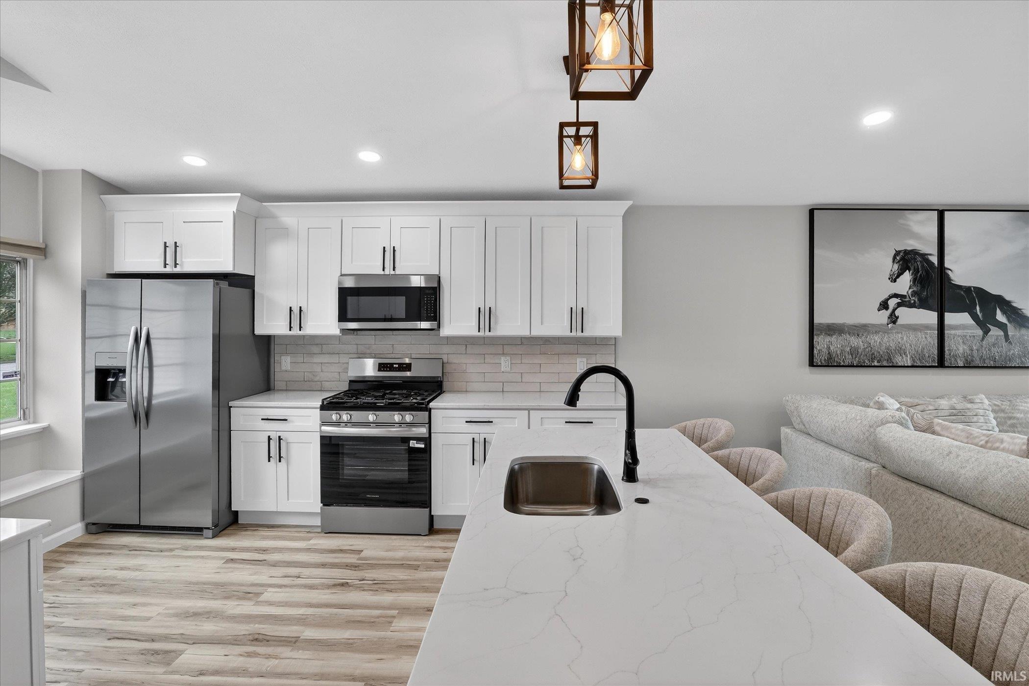Kitchen with stainless steel appliances, white cabinetry, and pendant lighting