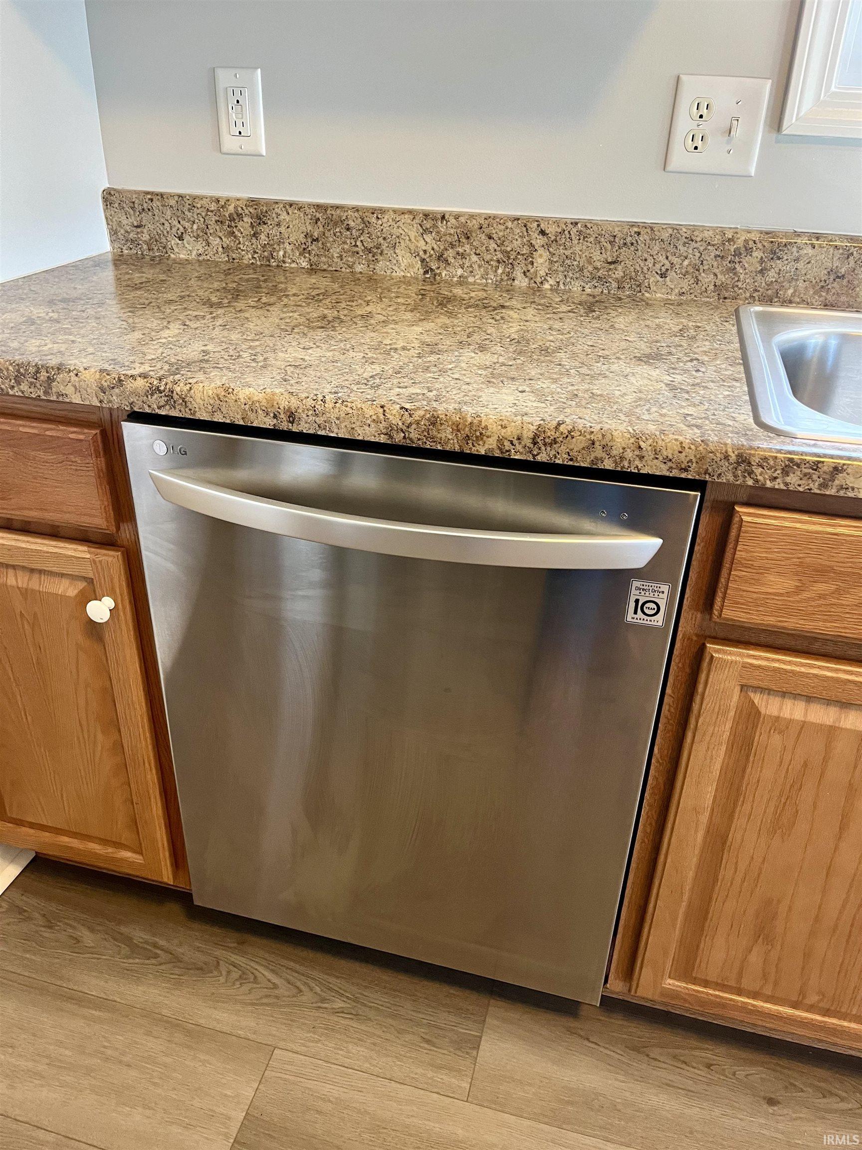 Kitchen view of stainless steel dishwasher, wood finish cabinets, and light wood-style floors