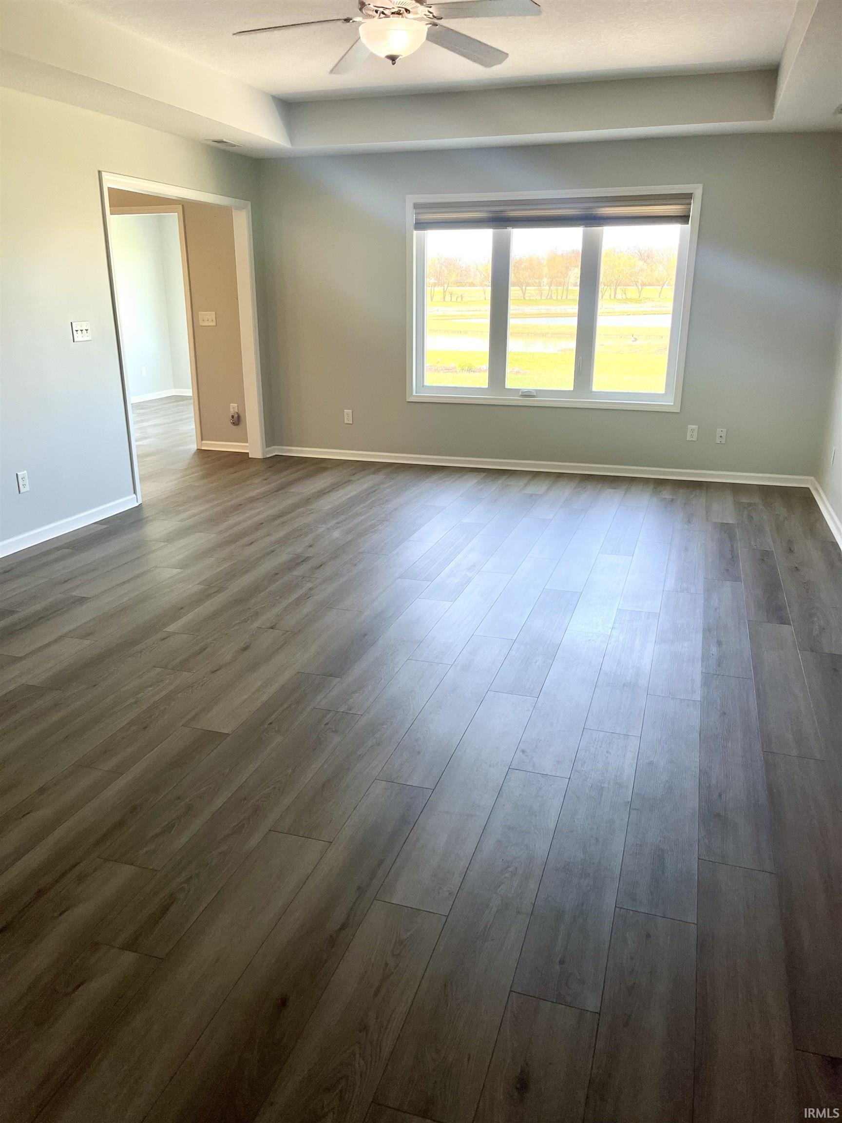 Unfurnished room featuring a ceiling fan, dark wood finished floors, and a raised ceiling